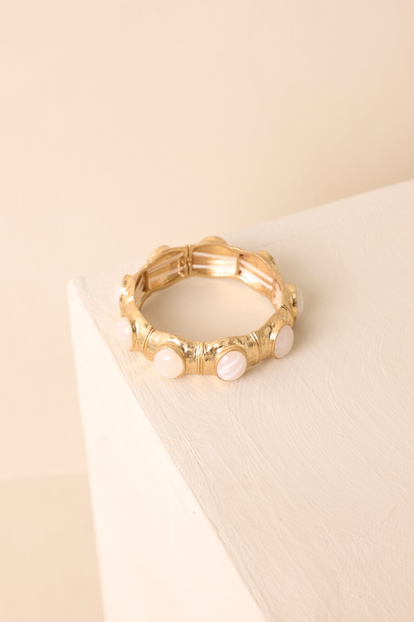 The stretch bracelet featuring ivory pearlescent oval stones in textured gold square frames shown against a beige background.