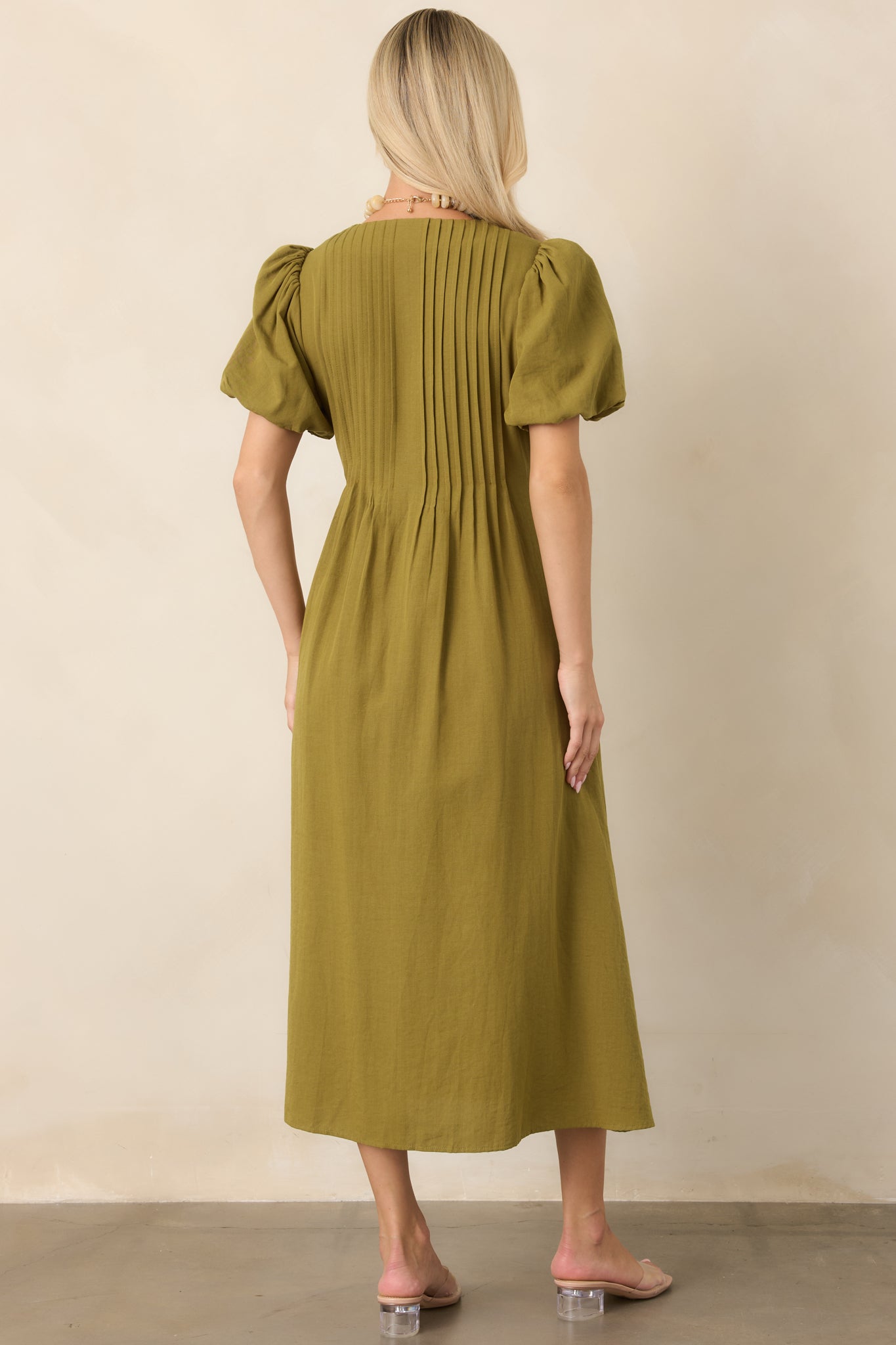 Rear view of the linen-textured midi dress showing the back pintuck detailing, softly gathered puff sleeves, flowing skirt, and clean concealed zipper finish.