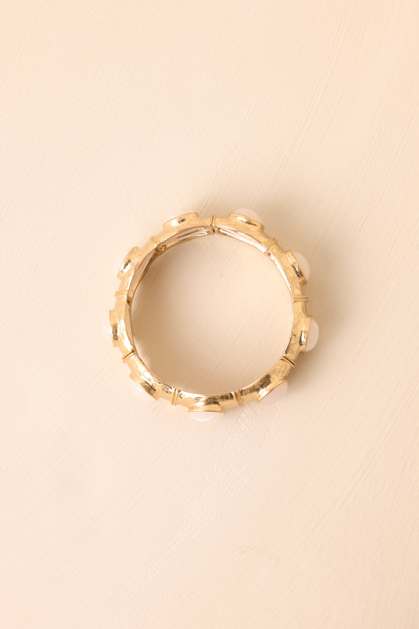 The stretch bracelet featuring ivory pearlescent oval stones in textured gold square frames shown against a beige background.