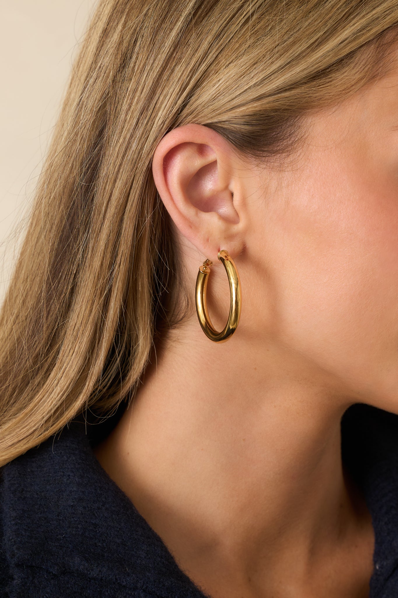 Cropped photo showing the thick gold hoop earrings with a rounded tubular shape and smooth polished finish.