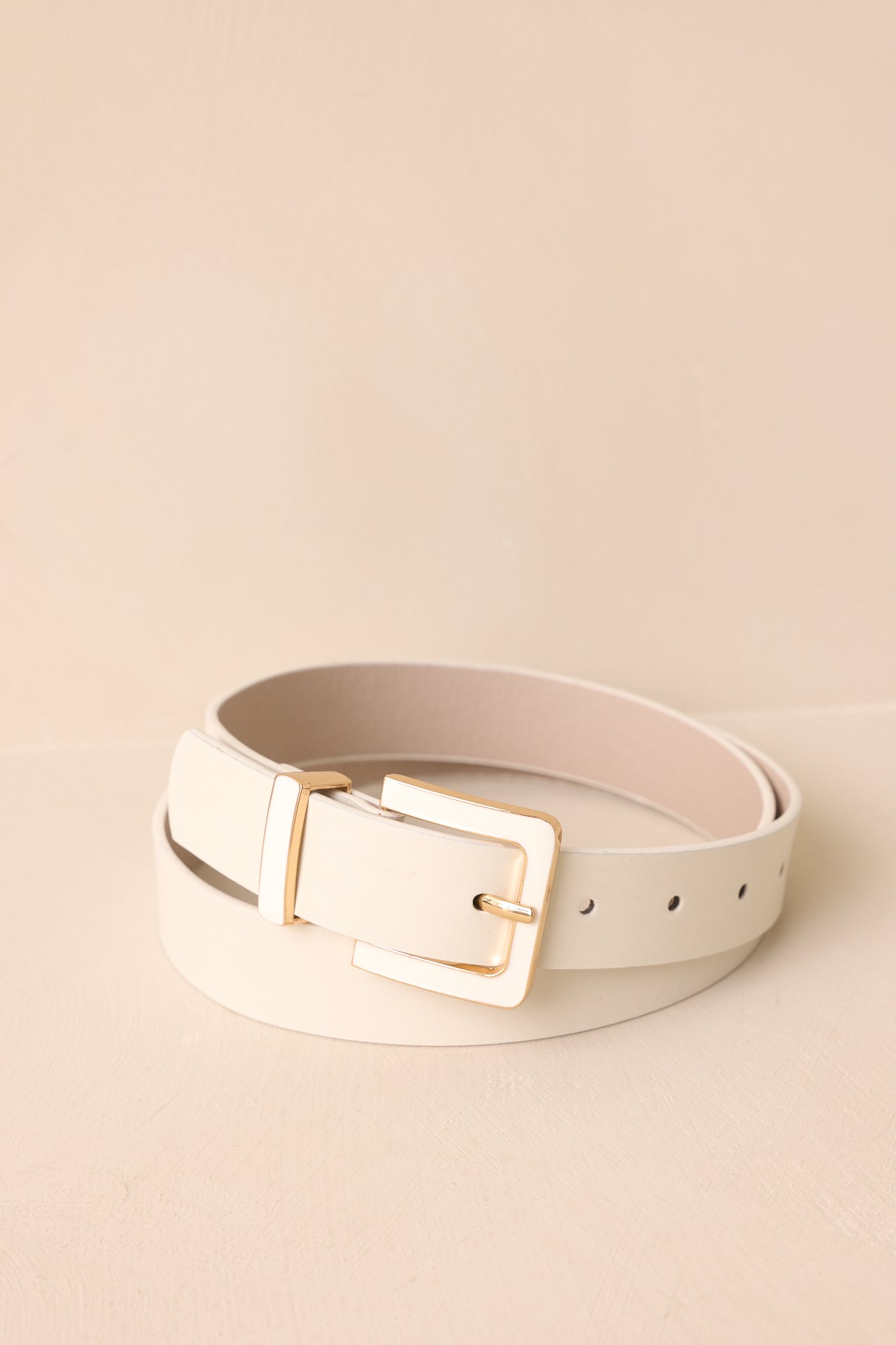Cropped view of a thick ivory belt with smooth material and a gold-bordered white buckle.
