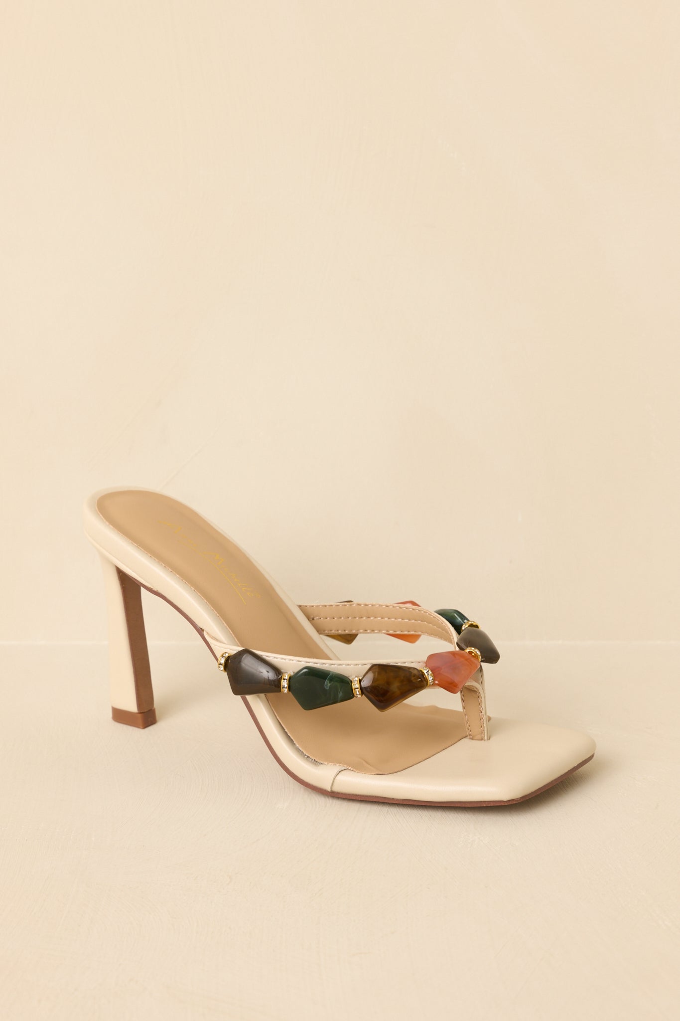 Three-quarter angle of heeled sandals on beige background emphasizing textured embellishment and silhouette