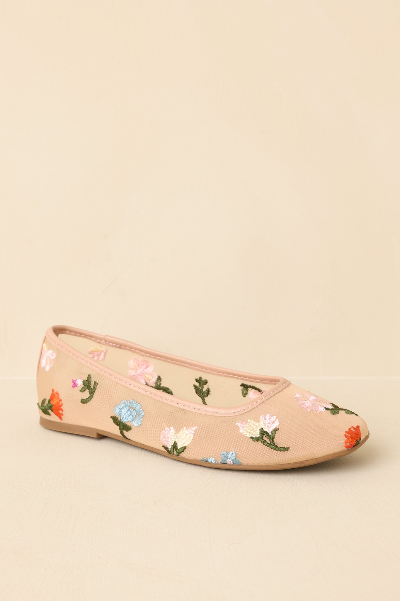 Three-quarter angle of nude embroidered flats on beige background emphasizing lightweight construction