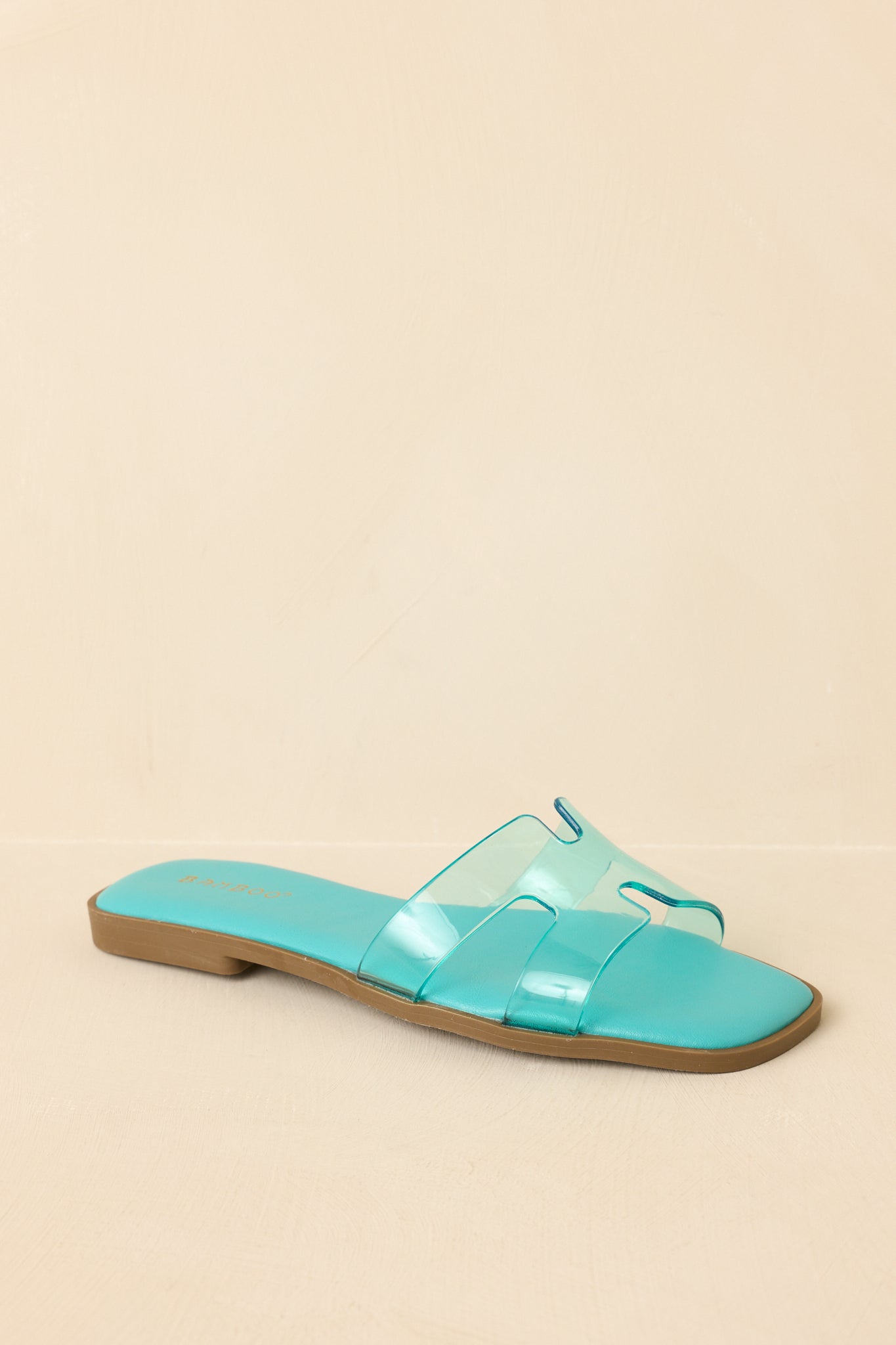 Three-quarter angle showcasing bright teal footbed and transparent strap design.