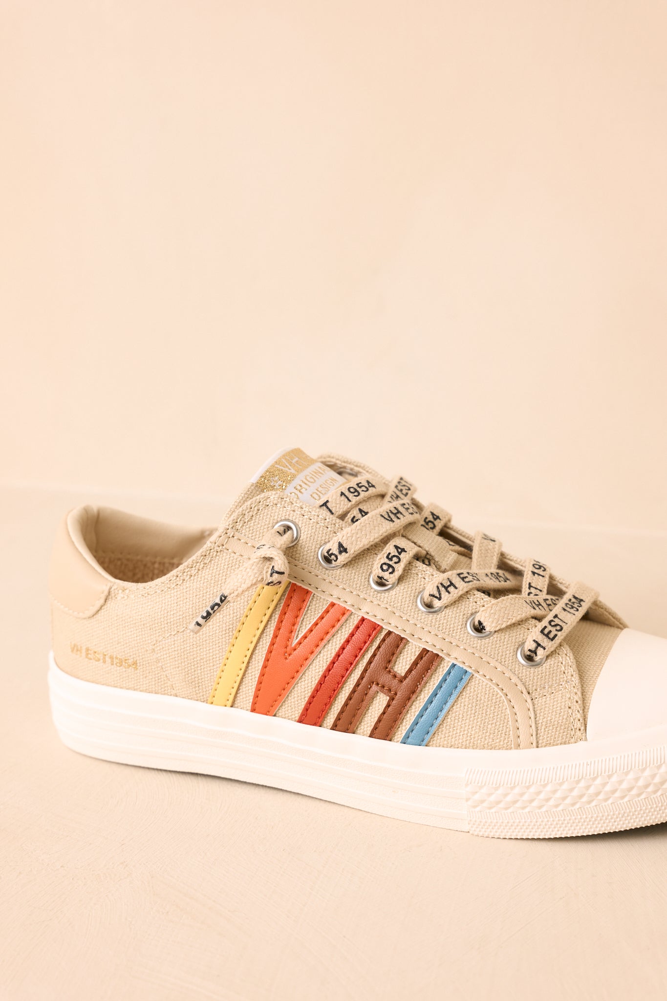 Nude canvas sneakers highlighted from a three-quarter angle, featuring colorful "VH" side panels and cushioned soles against a neutral beige setting.