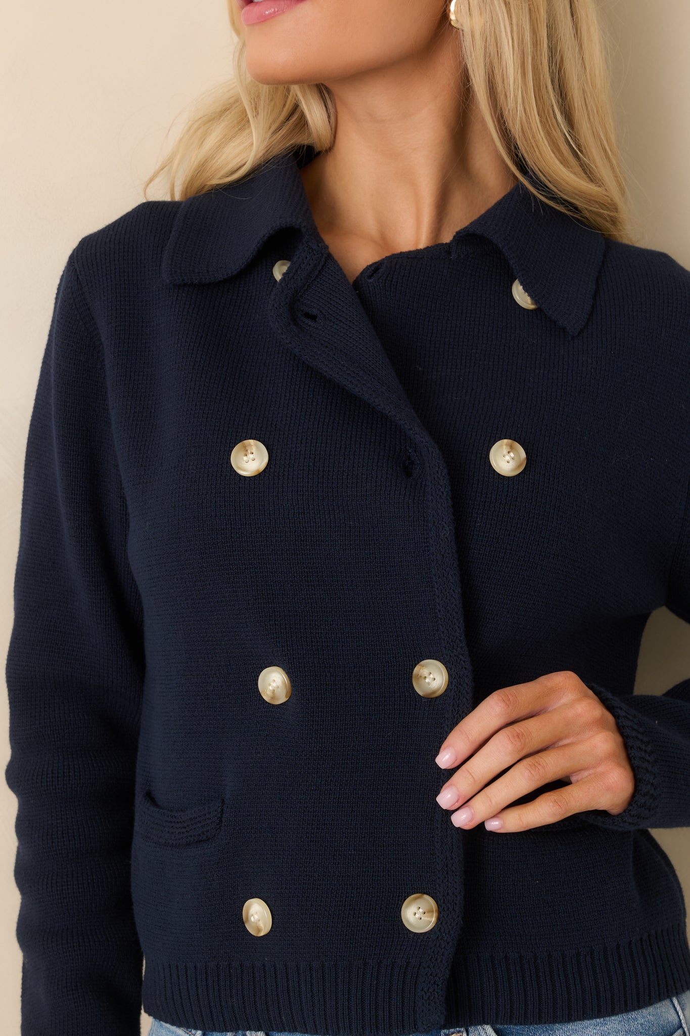 Tight detail of the ribbed cuff and button closure on the navy cotton knit cardigan, showing the soft knit construction.