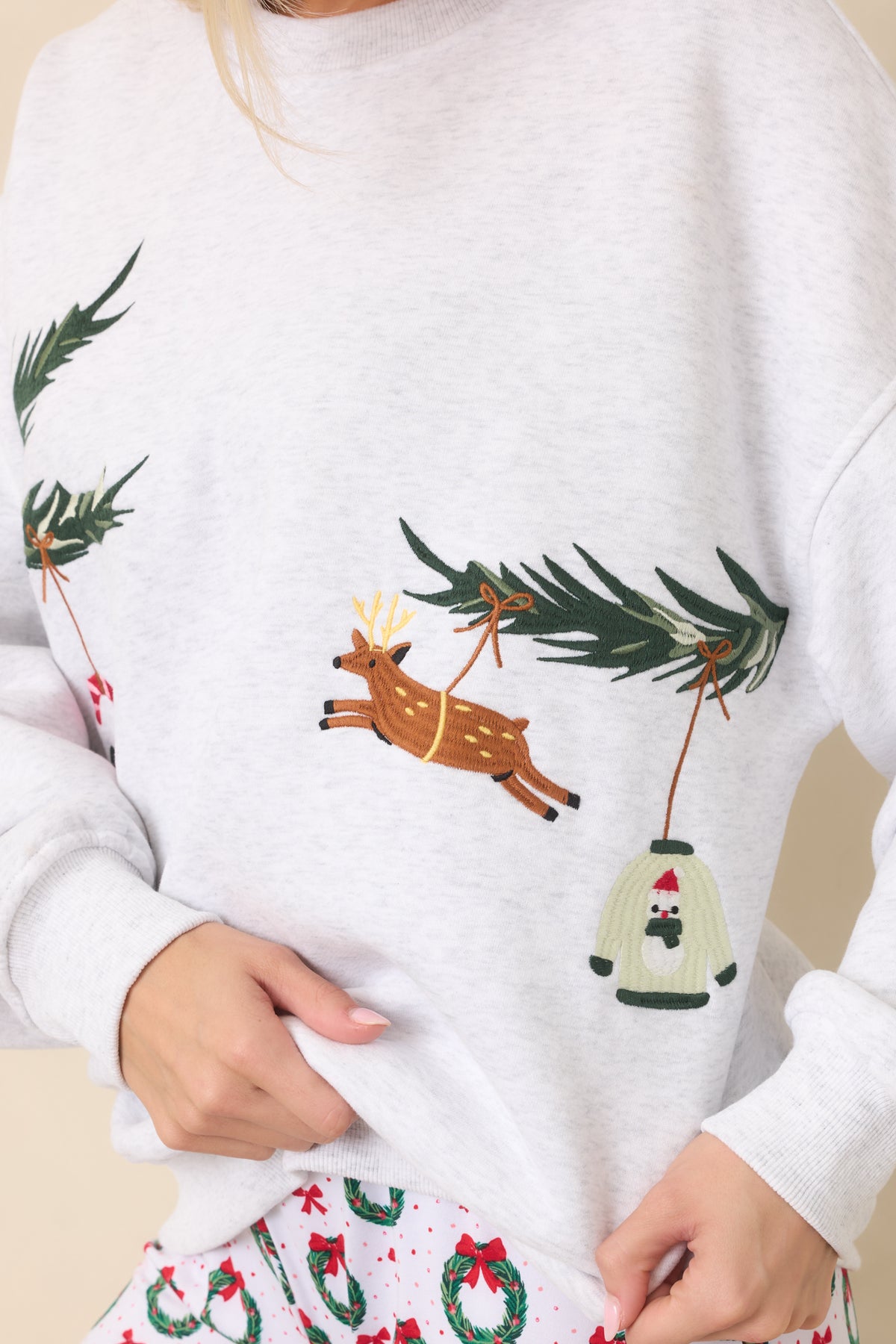 Detailed holiday embroidery featuring a tiny patterned Christmas sweater ornament and colorful decorations among green branches.