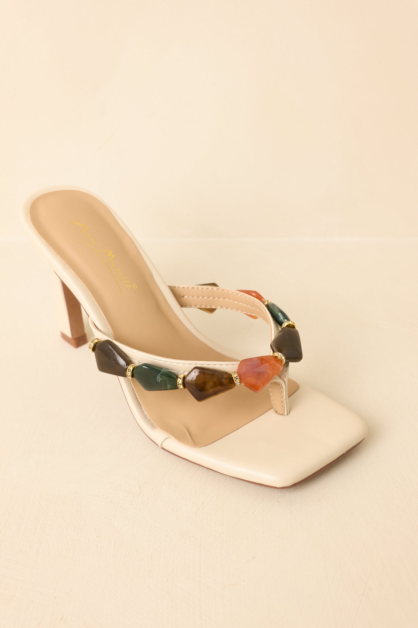 Top-down view of sandals on beige background featuring square toe and decorative stone strap