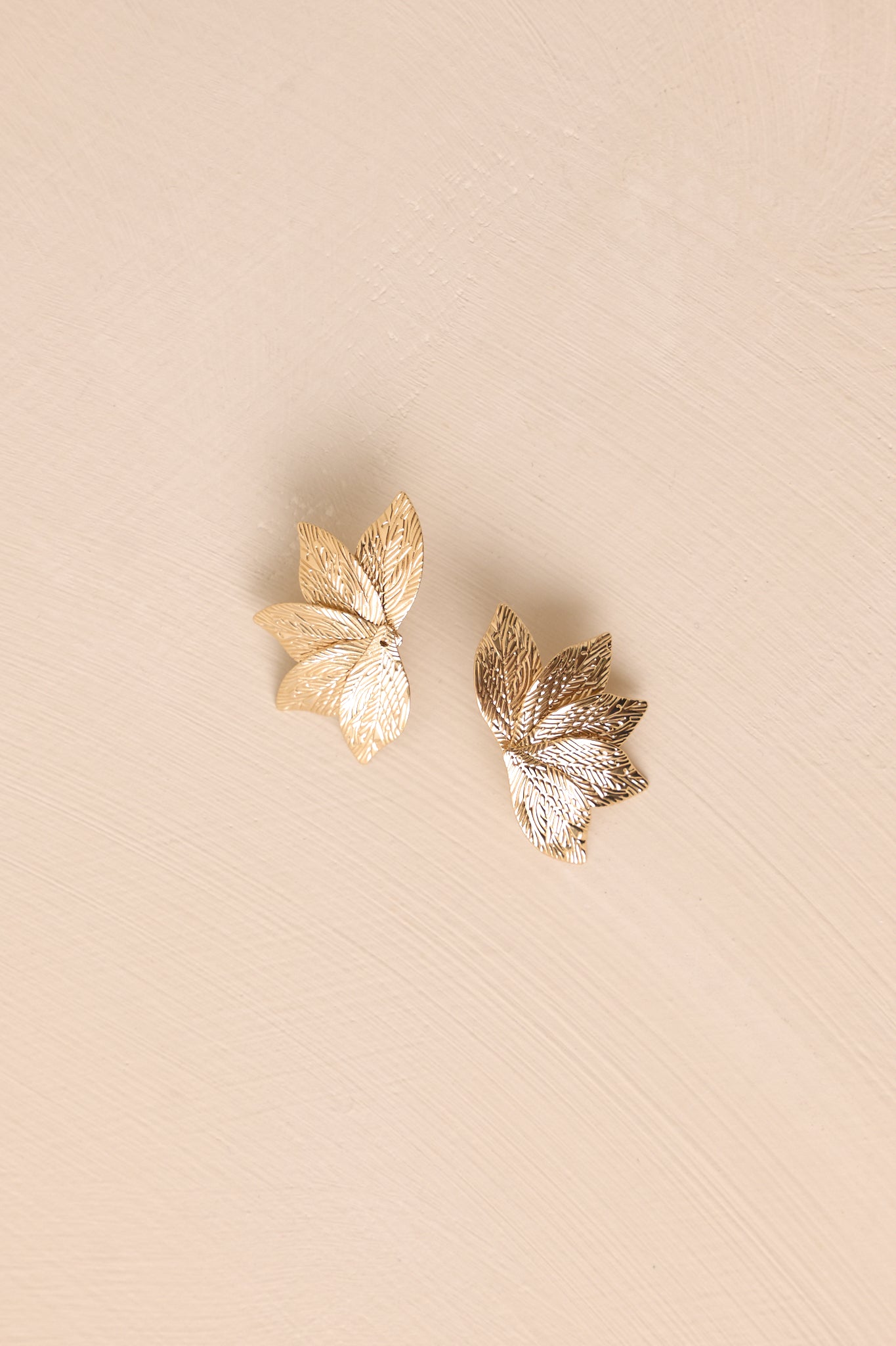 Top-down view of the gold earrings on a beige surface highlighting the polished leaf shape.
