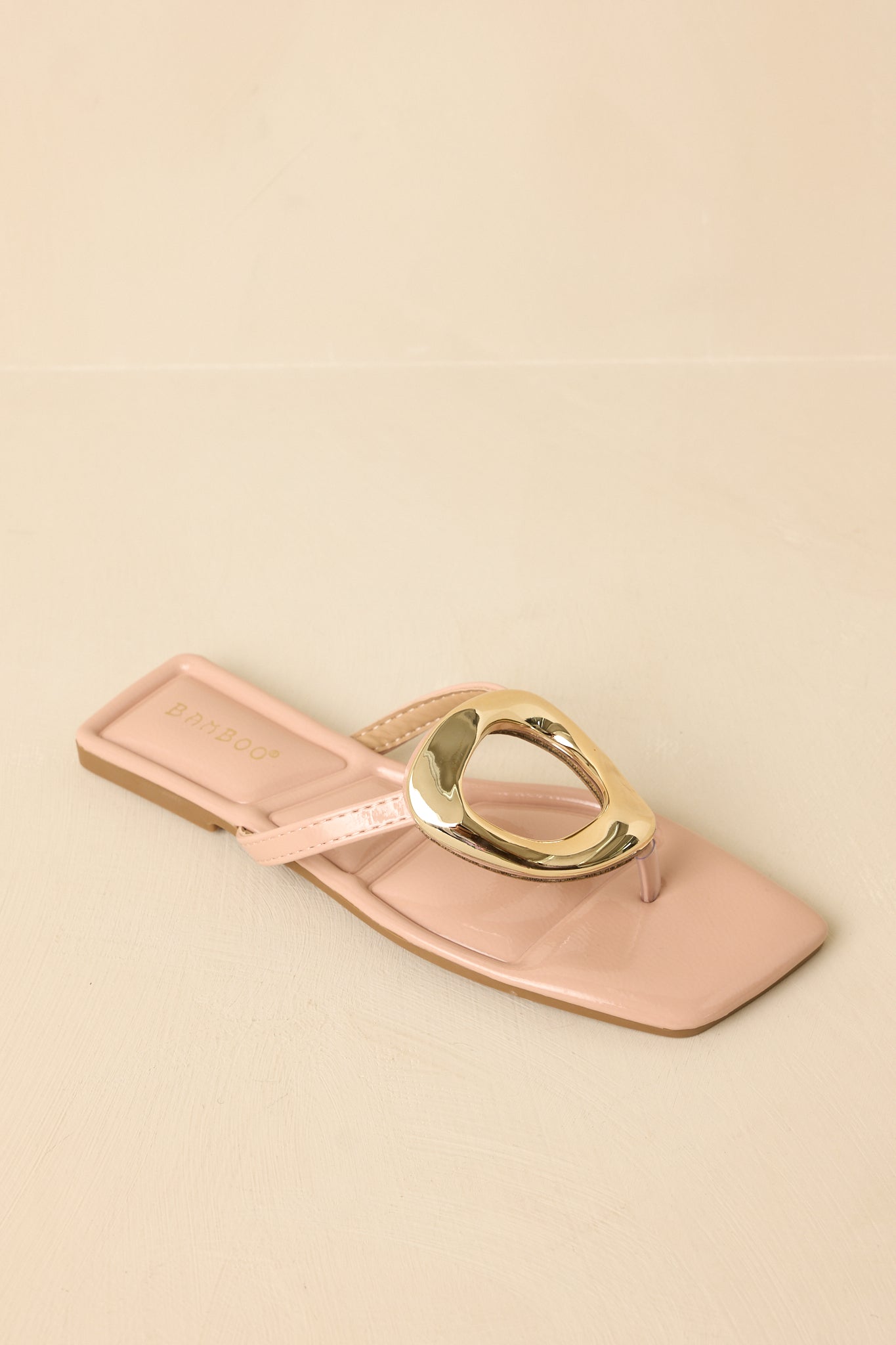 Top-down view of the nude patent sandals against a beige background highlighting the square toe and ring centerpiece.