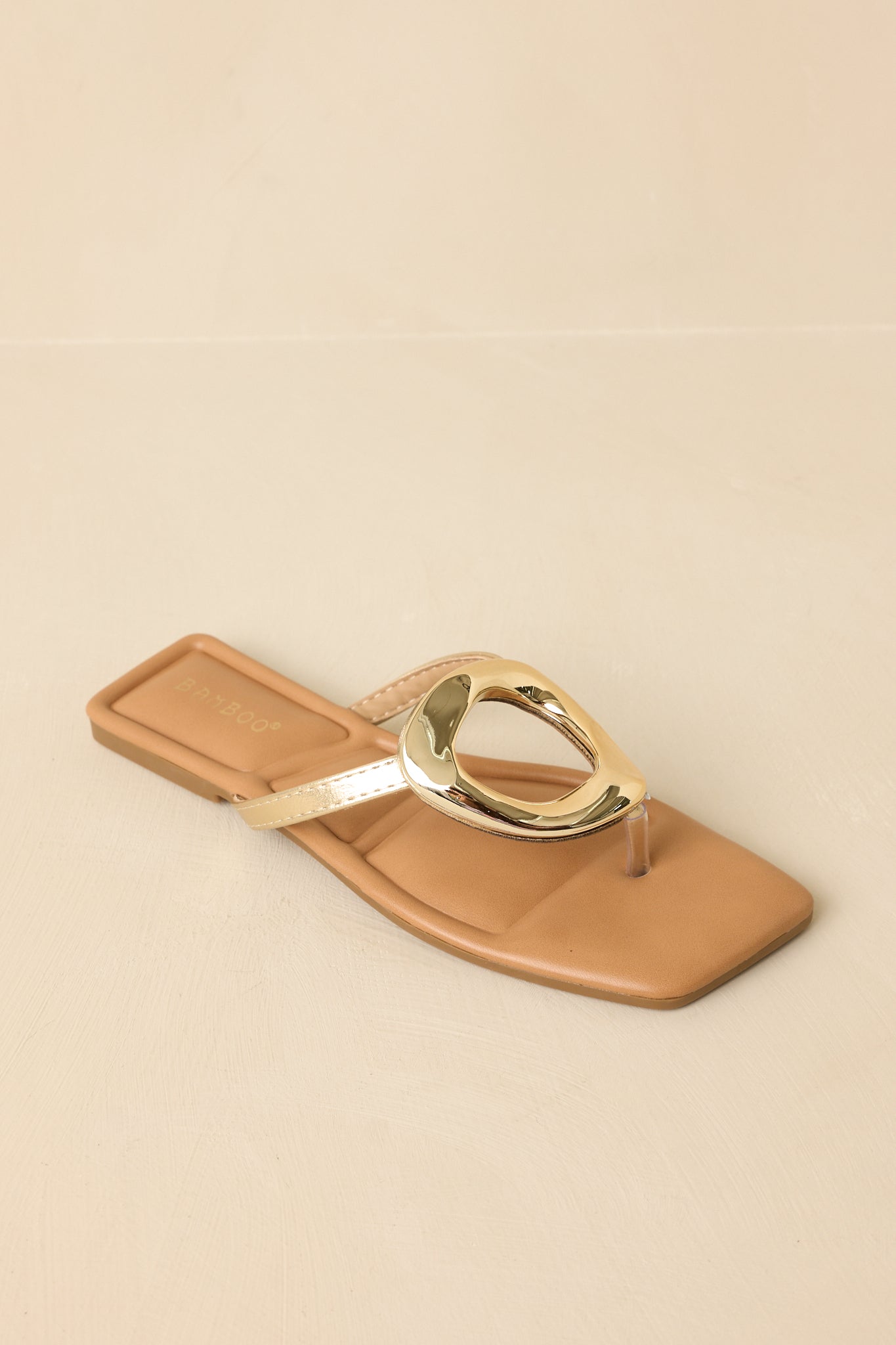 Top-down view of the gold metallic sandals against a beige background highlighting the square toe and ring detail.