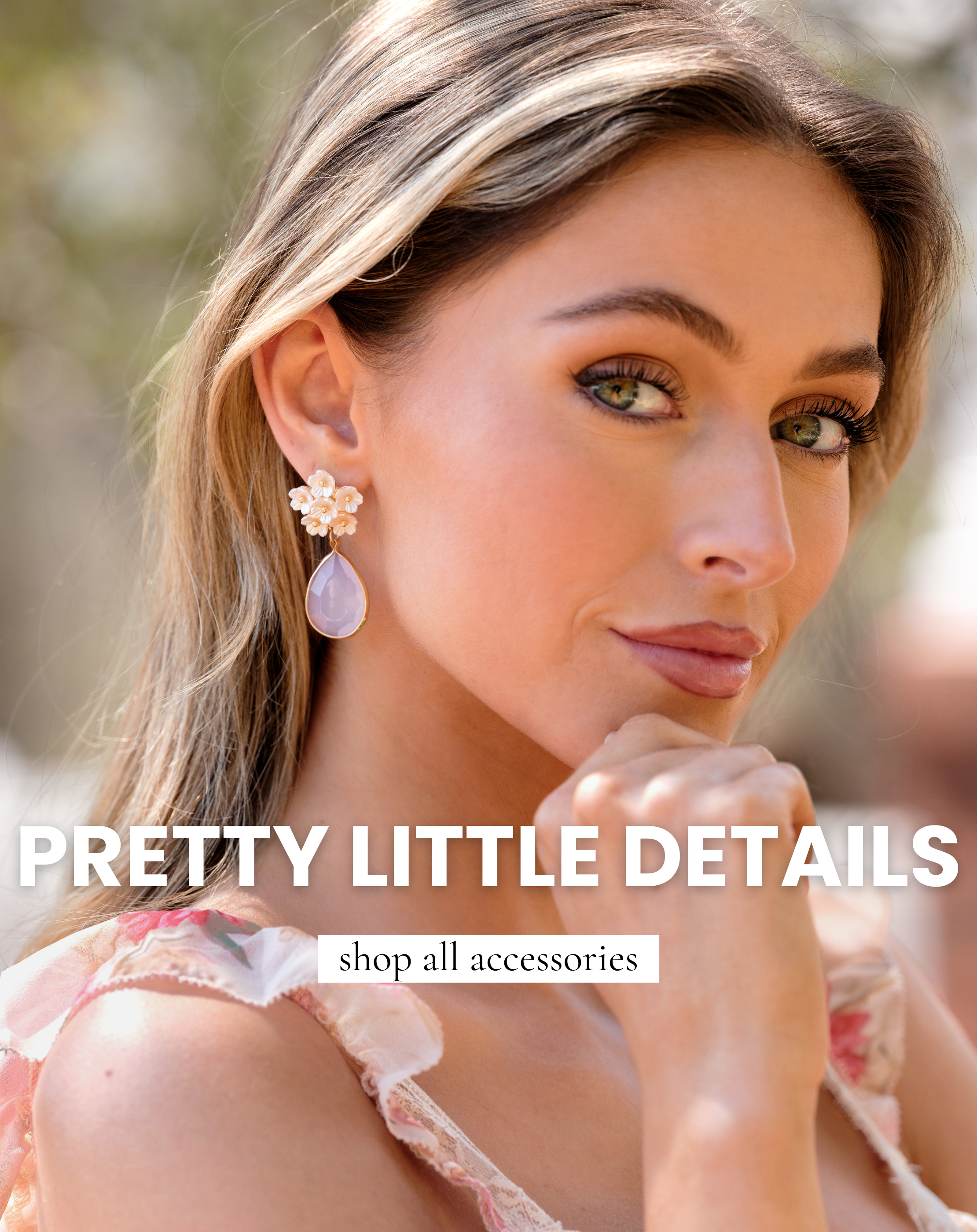 Model wearing floral drop earrings with a soft pink stone, styled with a feminine spring outfit, representing our accessories collection. This image leads to shop all accessories and highlights delicate, statement jewelry for spring styling.