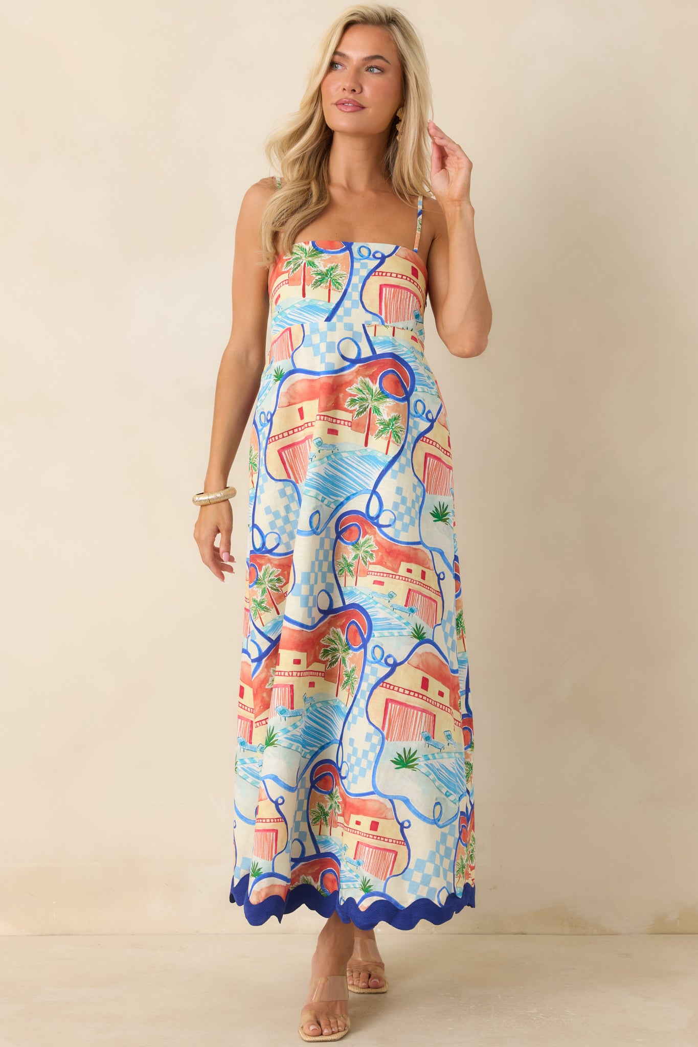Printed maxi dress showcasing a tropical poolside-inspired pattern, hidden side pockets, and a bold cobalt blue scalloped hem.