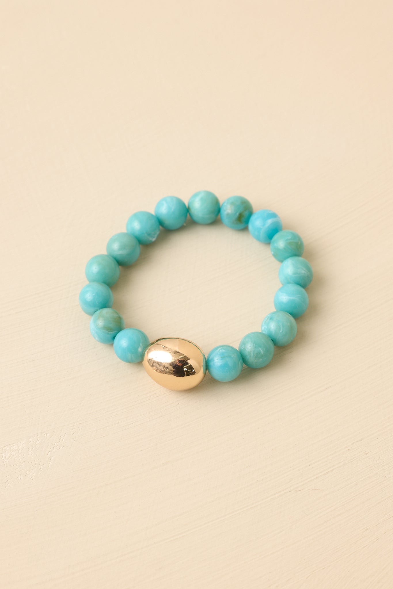 Turquoise beaded bracelet displayed against a beige background featuring smooth beads and a polished gold-tone detail.
