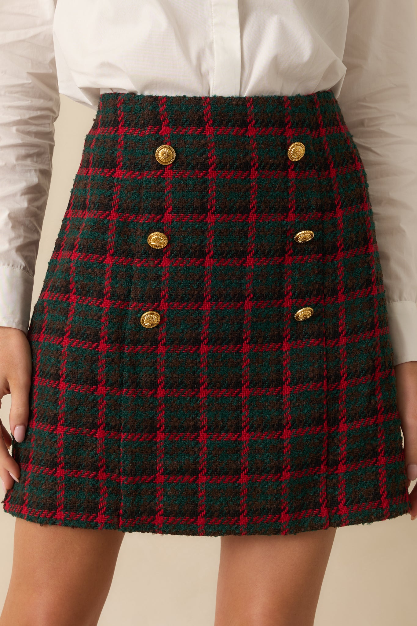 Tweed texture and double-breasted button design emphasizing the skirt’s high-waisted construction.