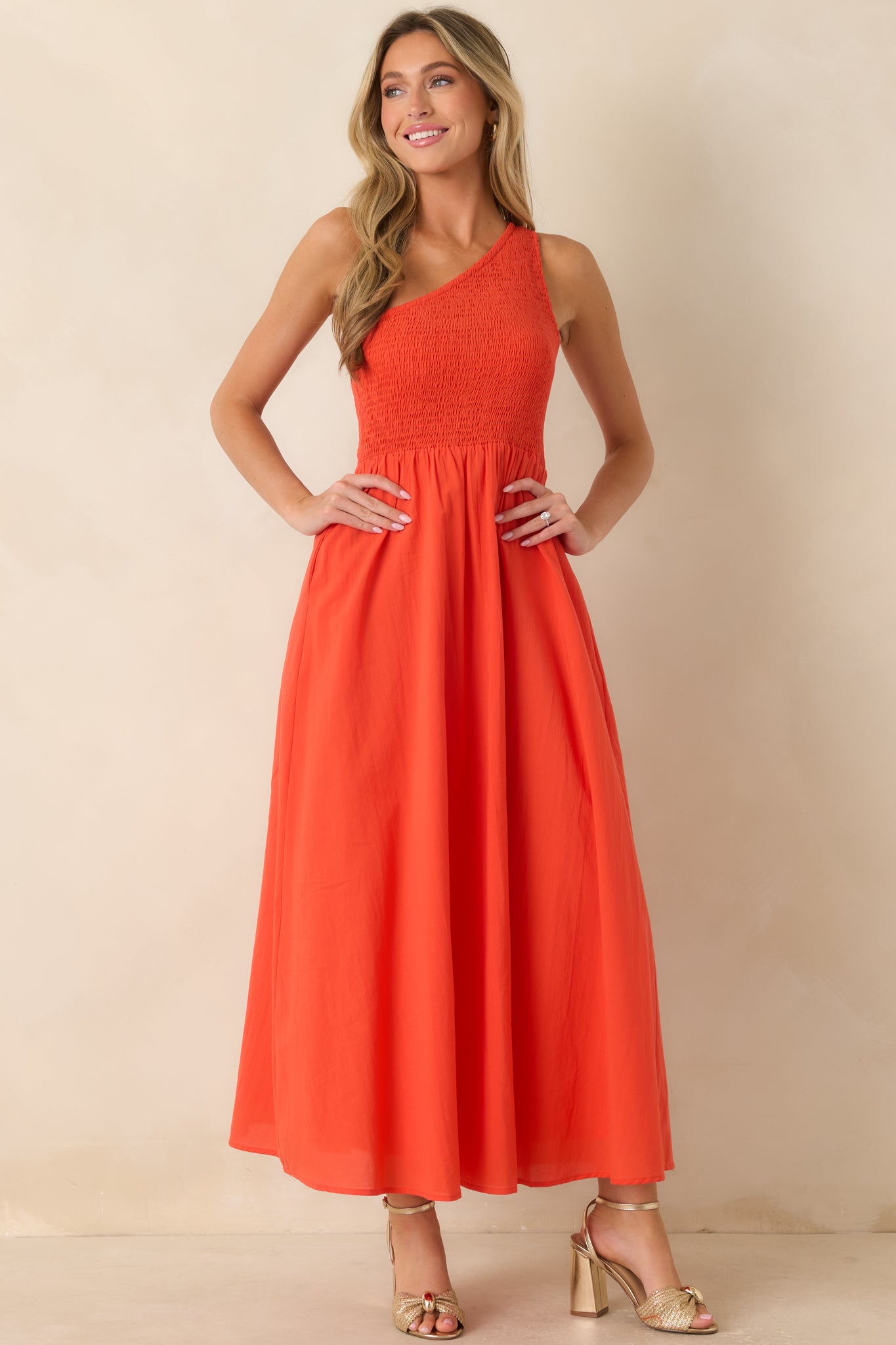 Vibrant coral-orange maxi dress showcasing a textured smocked bodice, asymmetrical one-shoulder design, and a breezy A-line silhouette.