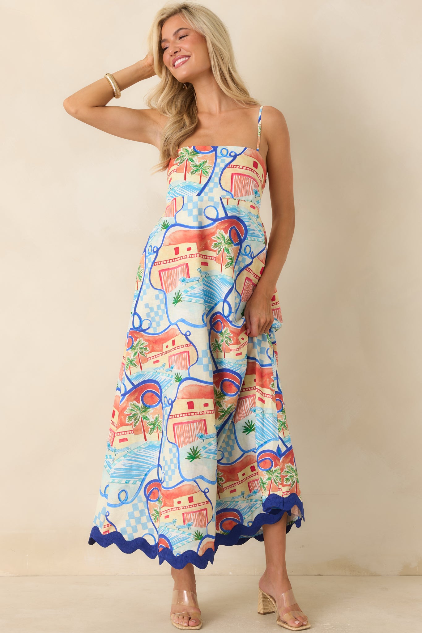 Vibrant scenic print maxi dress featuring palm trees, coastal architecture, adjustable spaghetti straps, and a flowing silhouette.