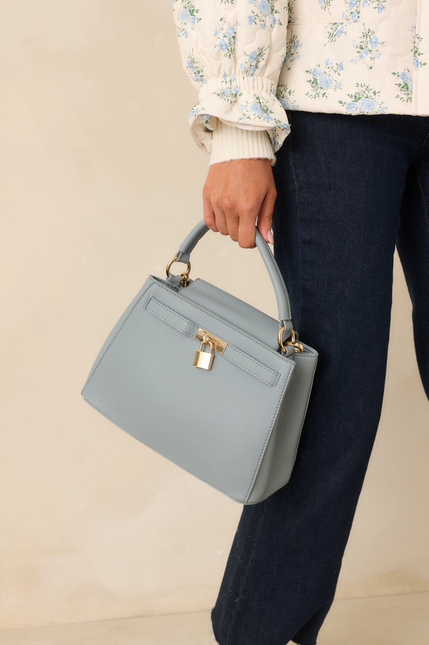 Cropped front view focusing on the smooth faux leather texture and flap closure of the dusty blue handbag.