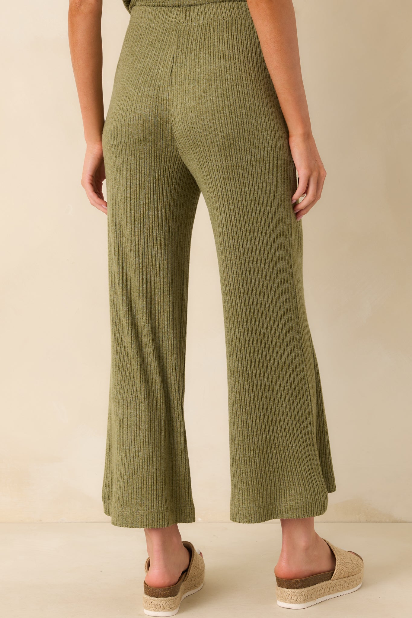 A view from behind of the olive green pants showing the high rise waist, elastic band, and wide leg flow