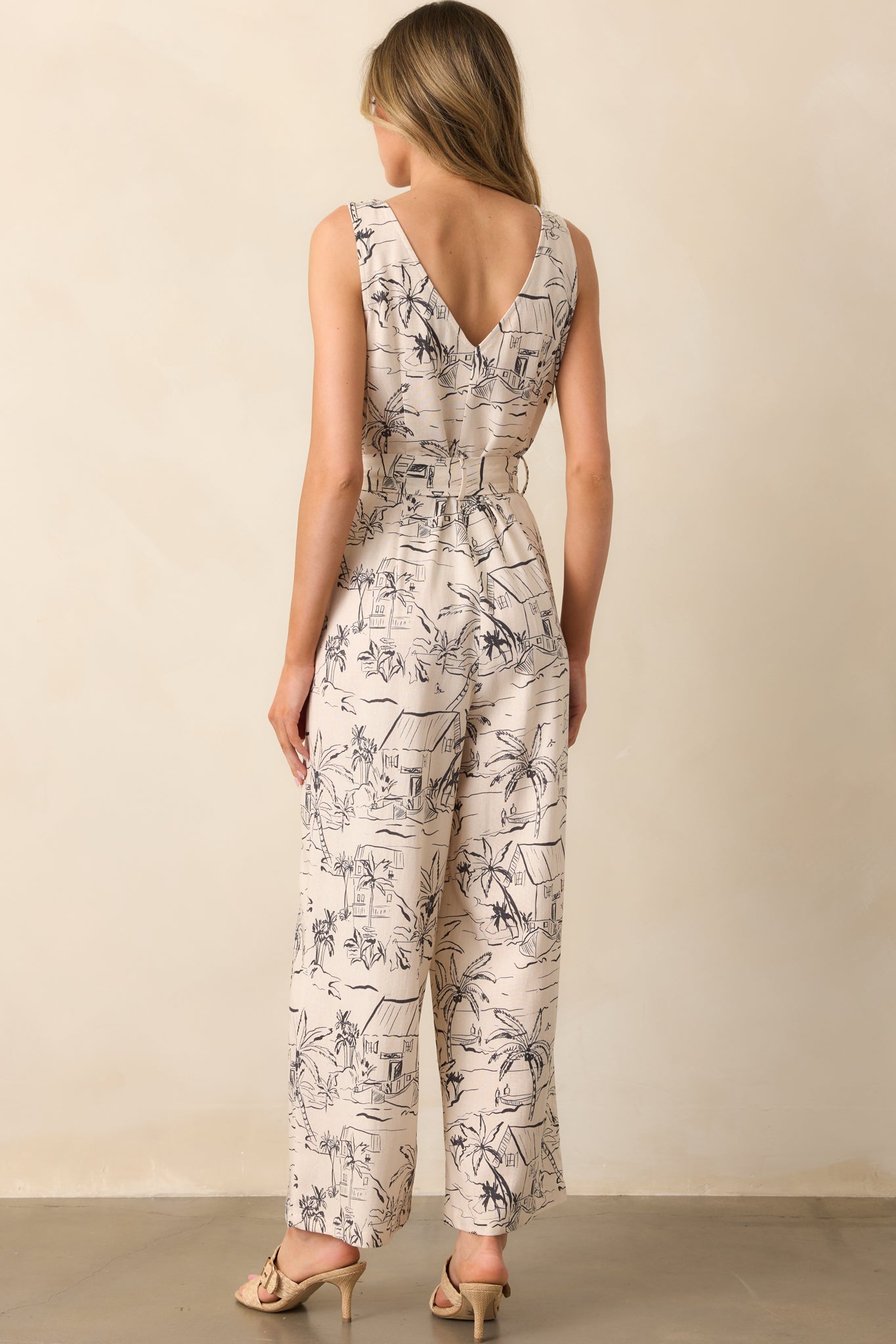 A view from behind showing the sleeveless design, button details, and the flowing fit of the ivory jumpsuit.