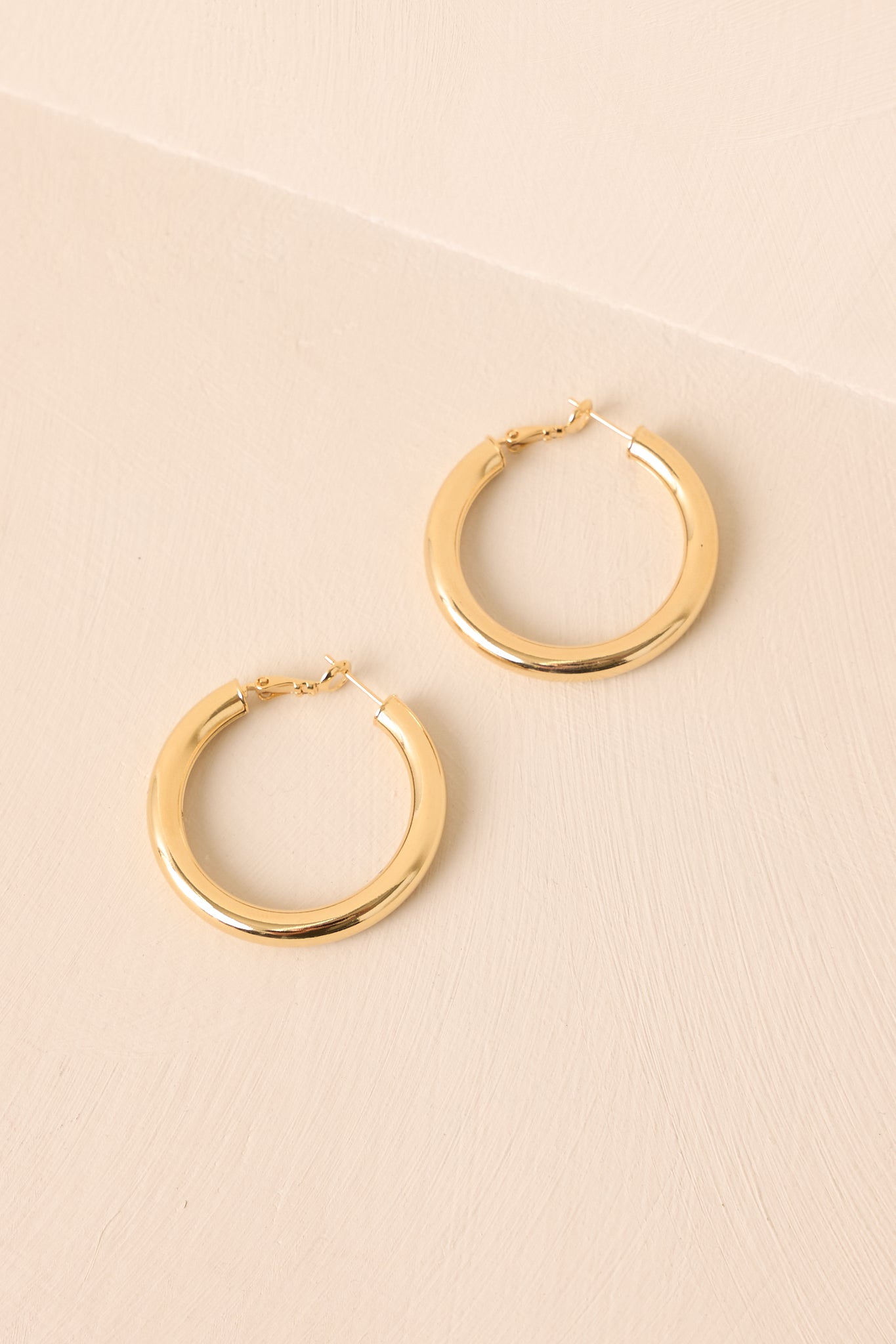 Cropped angled view of the gold hoop earrings showing the tubular design and hinge clasp detail.