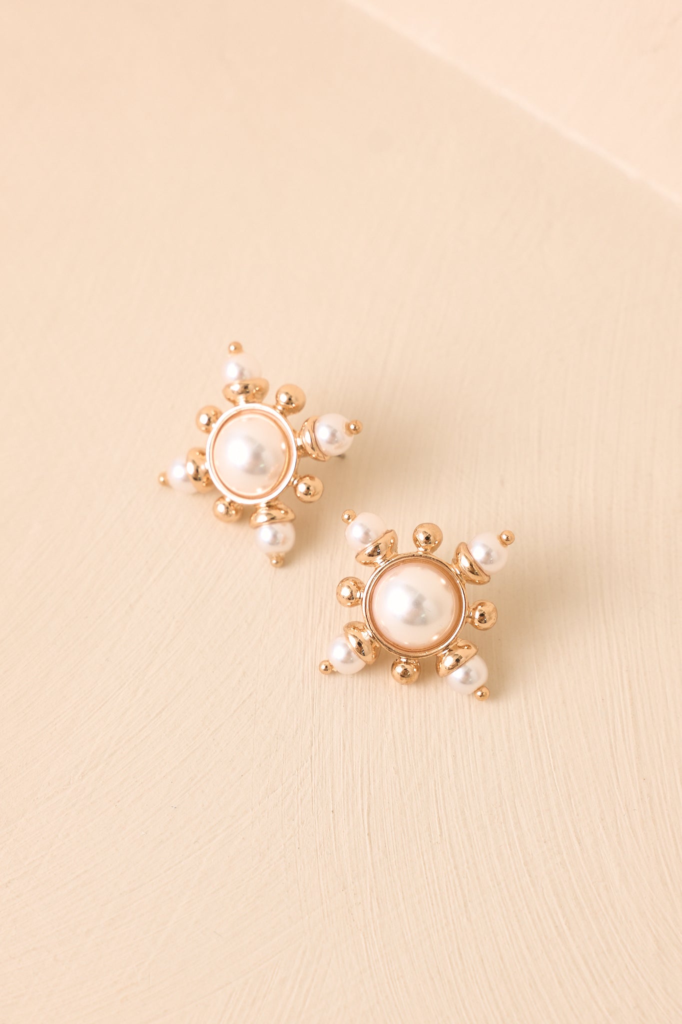 Vintage-inspired pearl earrings on a beige background featuring a luminous center and polished gold finish.