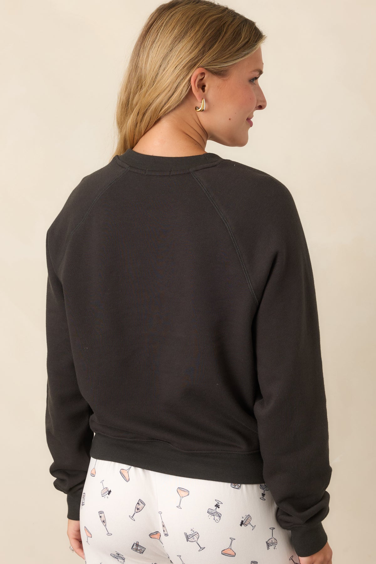 Rear view of the washed black sweatshirt showing the plain back, raglan sleeves, crew neckline, and ribbed trim.