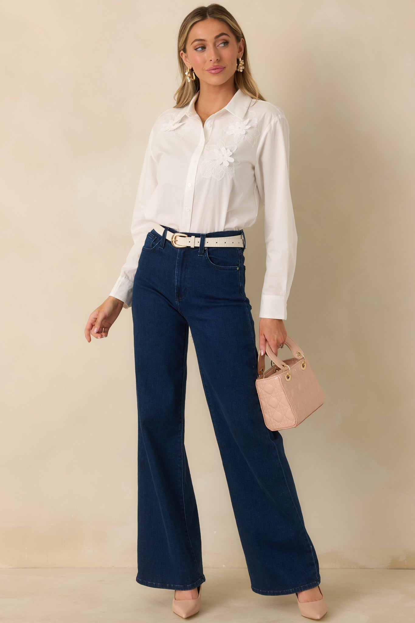 White woven button-up blouse with floral appliqué detail along front, shown fully buttoned with a relaxed, untucked fit.

