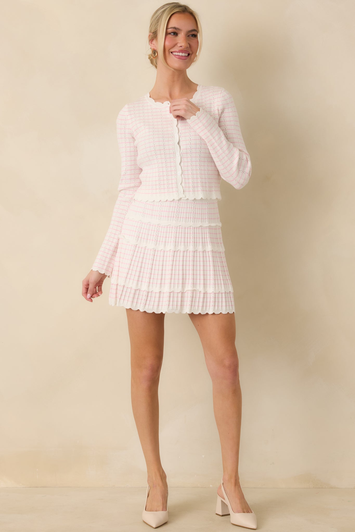 White cardigan with a pink stripe pattern, featuring a round neckline, scalloped trim, and functional button-up front.