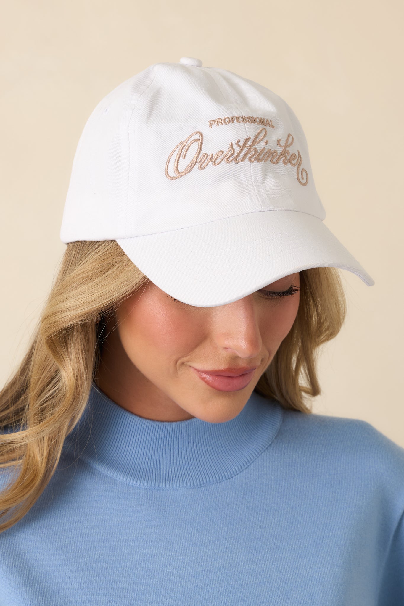 White cotton baseball cap with curved brim and embroidered “Professional Overthinker” lettering on the front.
