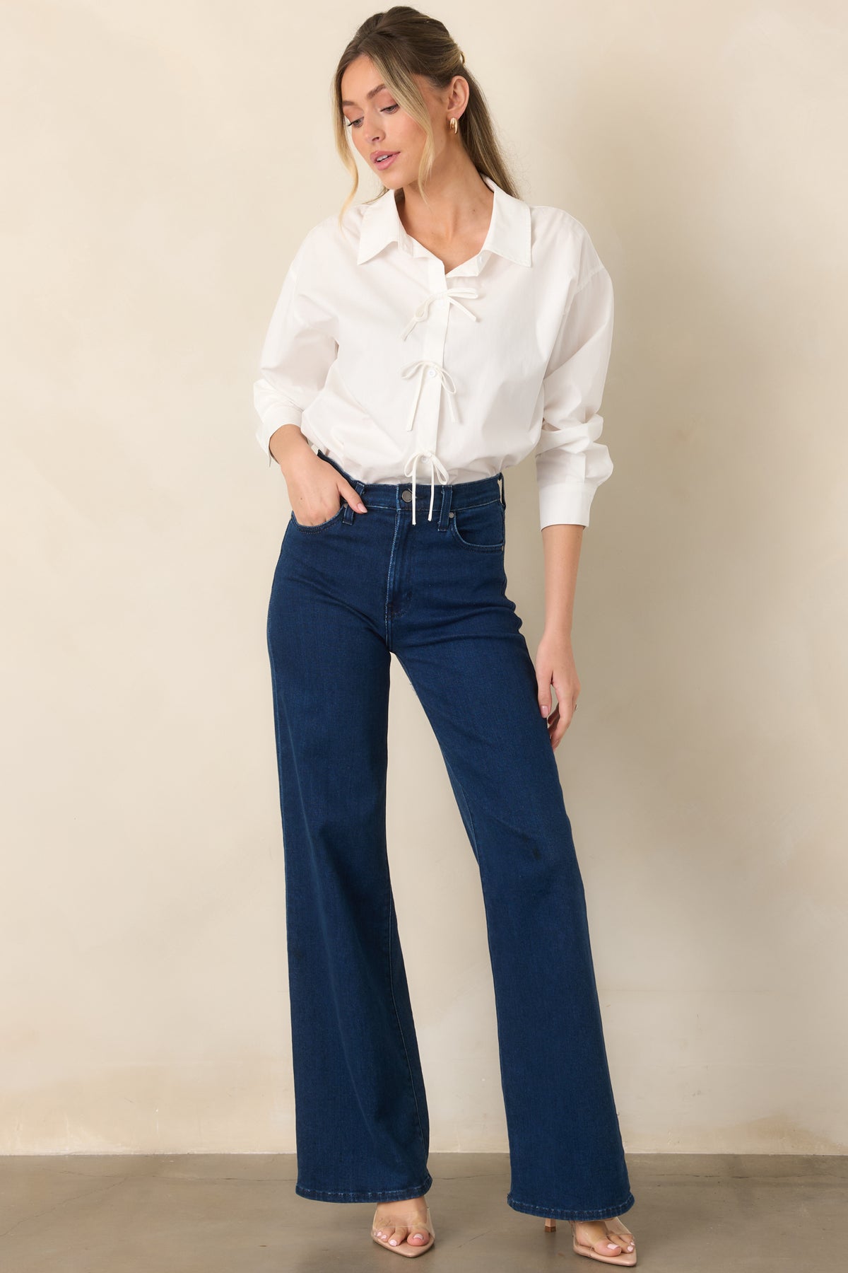 Crisp white cotton blouse with a structured collar, functional button placket, long sleeves, and feminine bow accents decorating the front.