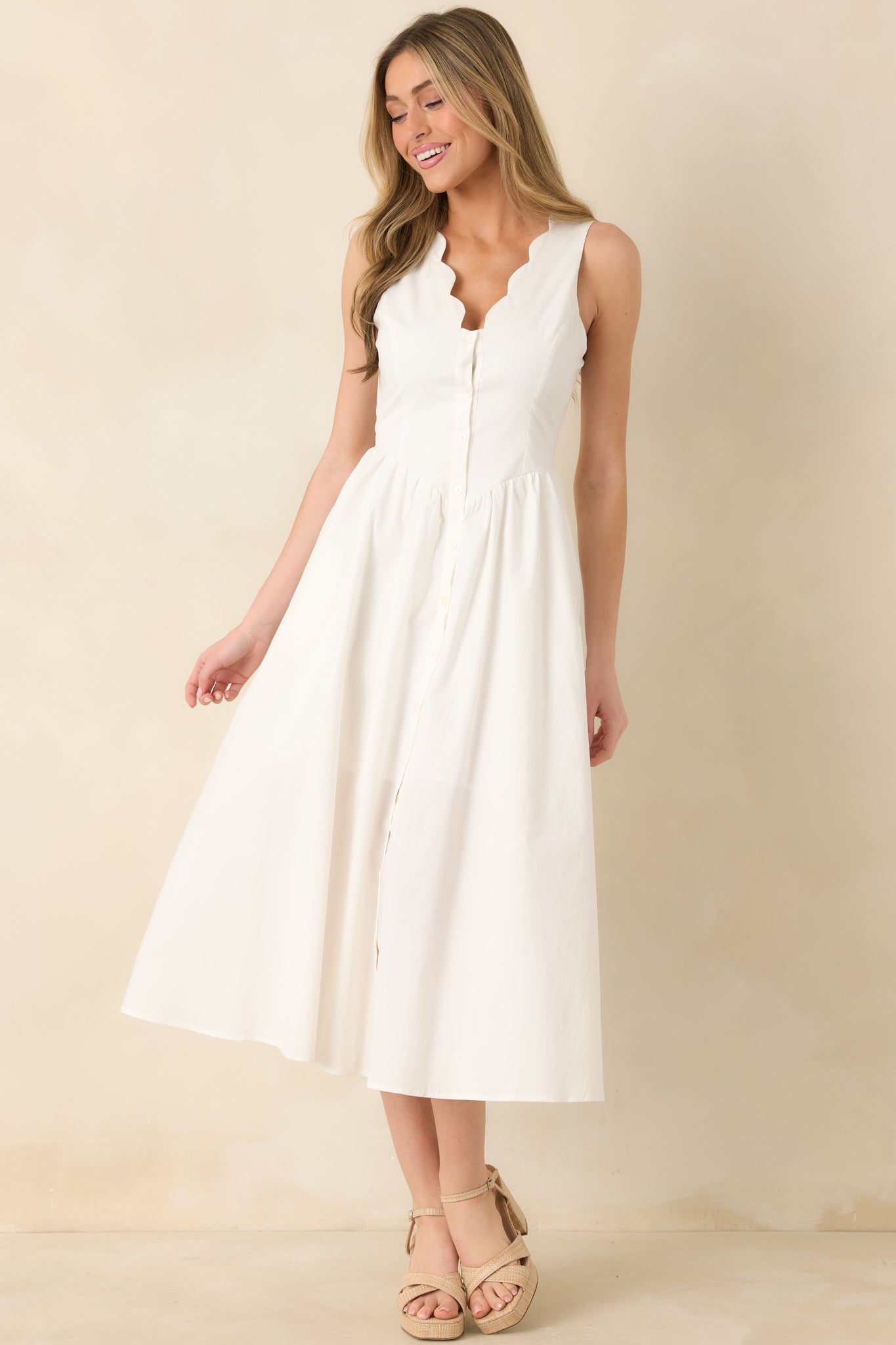 White cotton midi dress with a V-neckline, scalloped trim along the straps, a fitted bodice, and a button-front skirt that falls to a breezy midi length.
