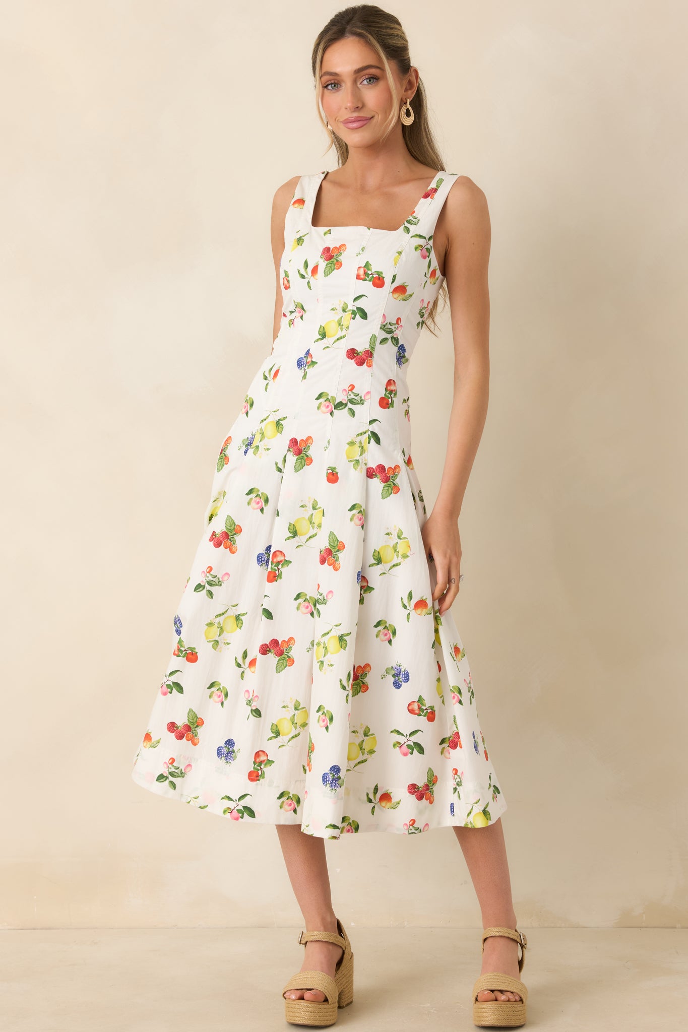 White cotton midi dress with colorful fruit print, fitted bodice seams, and soft pleated skirt