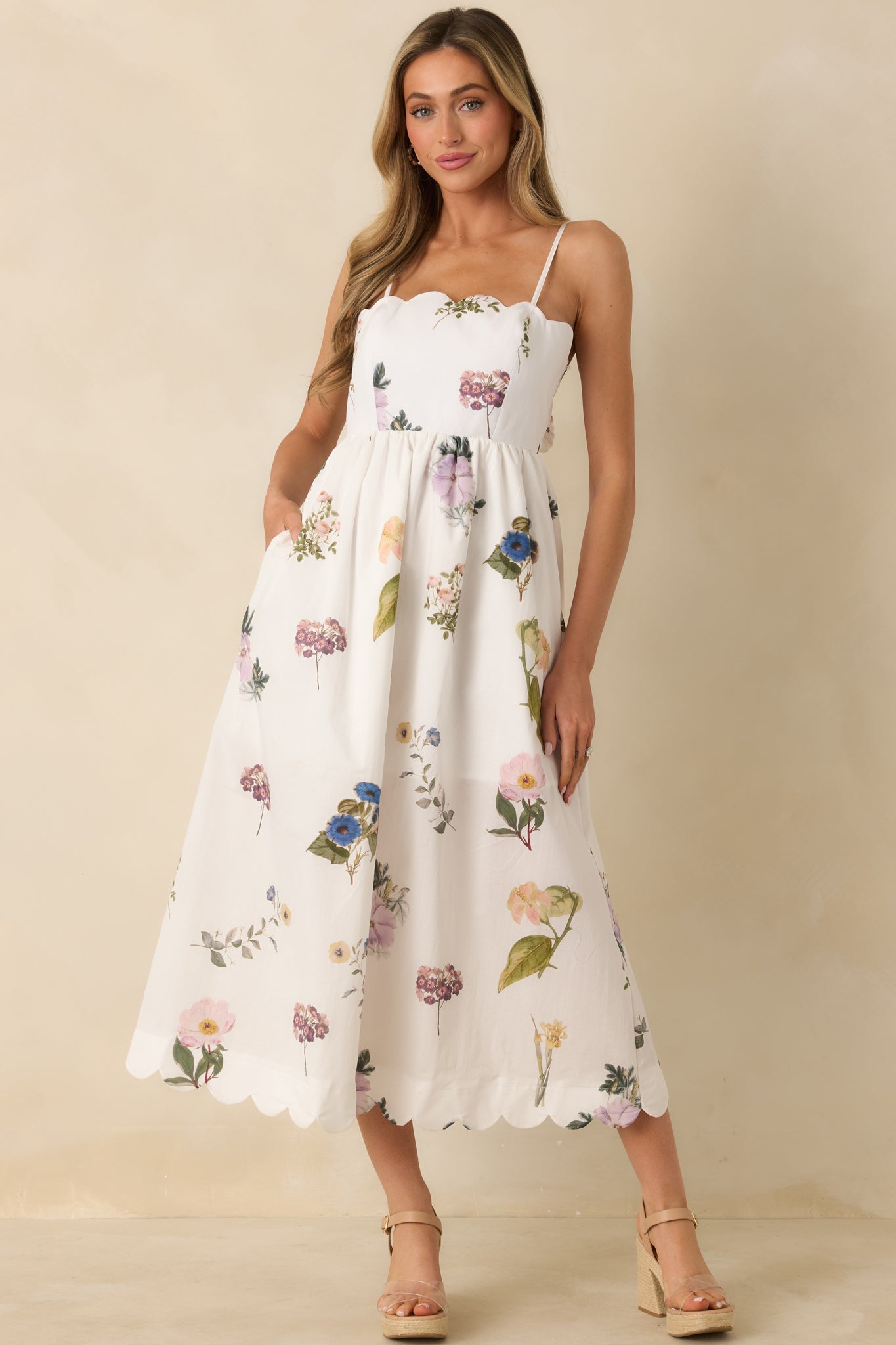 White cotton midi dress with multicolor floral print, scalloped neckline, adjustable spaghetti straps, and flowy skirt.