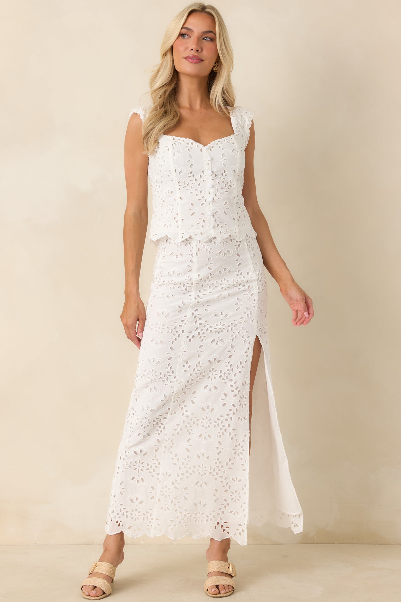 White eyelet maxi skirt with a high-waisted design, side slit, and delicate embroidered floral pattern throughout.