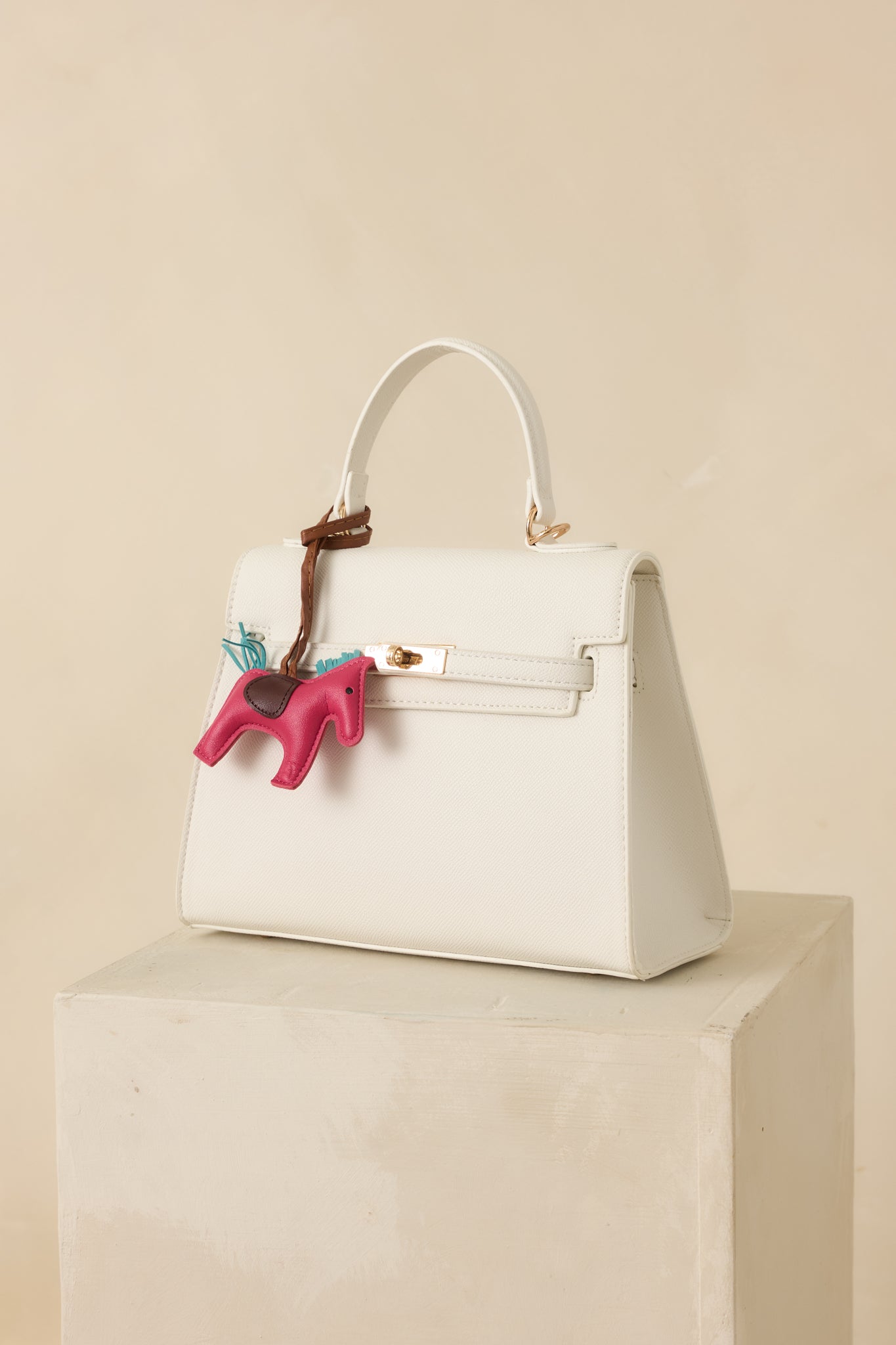 White faux leather handbag with structured silhouette, top handle, and front flap secured by overlapping straps and twist lock.