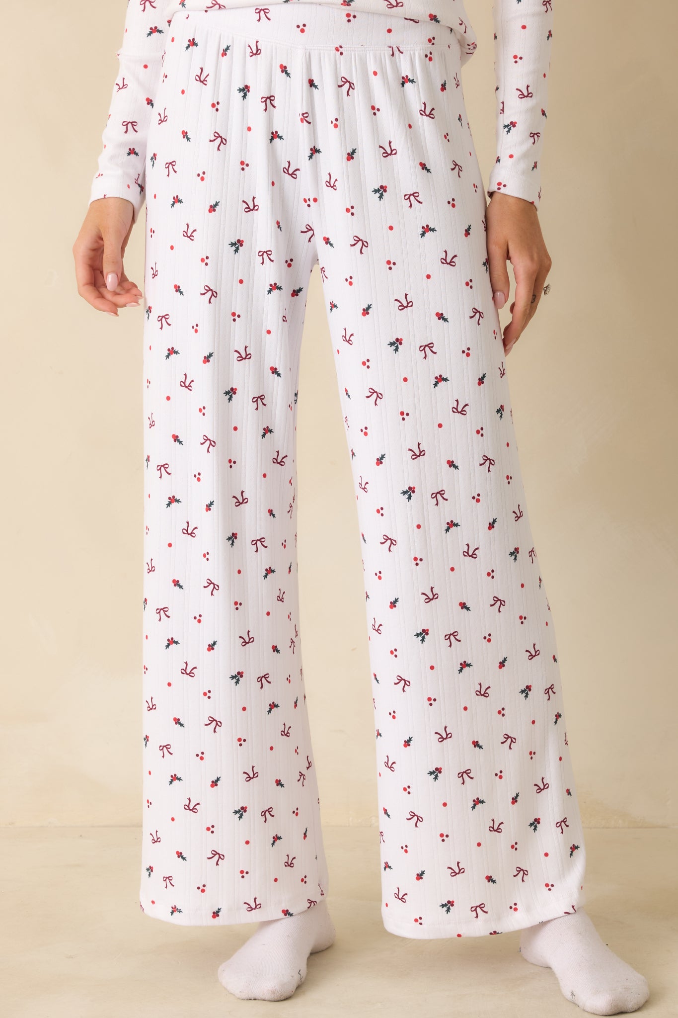 White full-length pants with a wide-leg fit, high-rise elastic waistband, and allover holly-and-bow print in silky Pointelle knit.