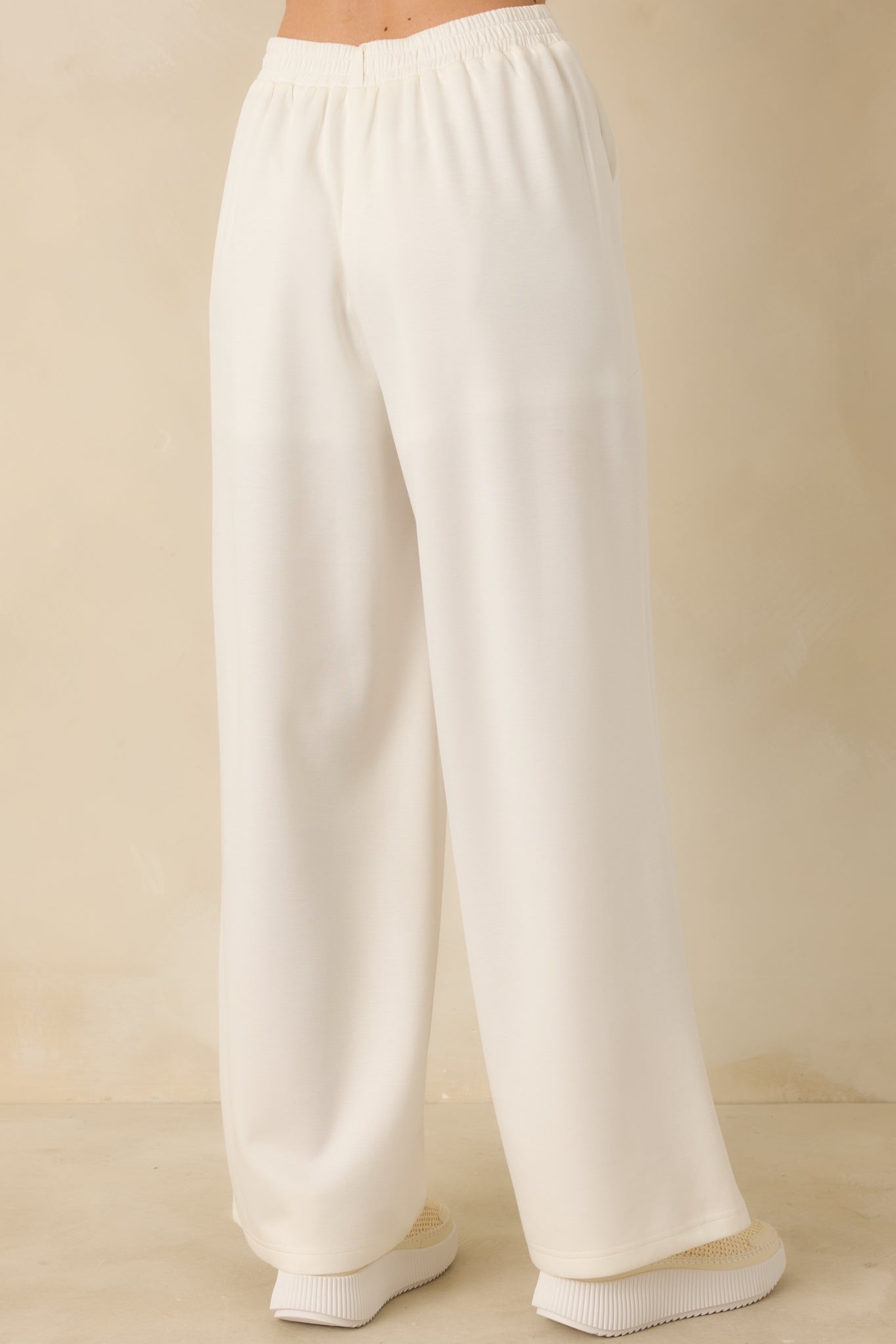 White high-waisted pants displaying the wide-leg silhouette from the rear with a smooth knit finish and clean lines.