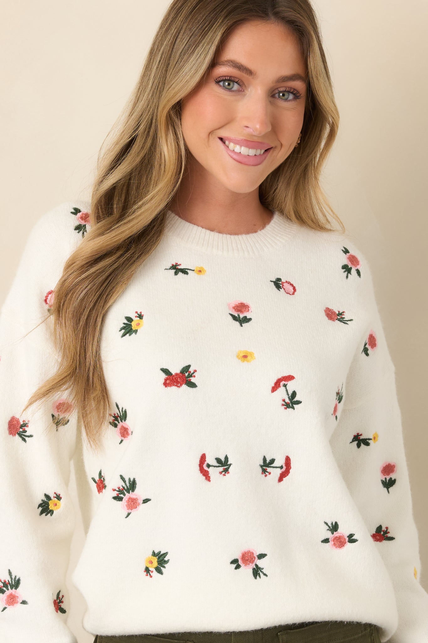 Close view of the white knit sweater highlighting colorful floral embroidery across the textured fabric.
