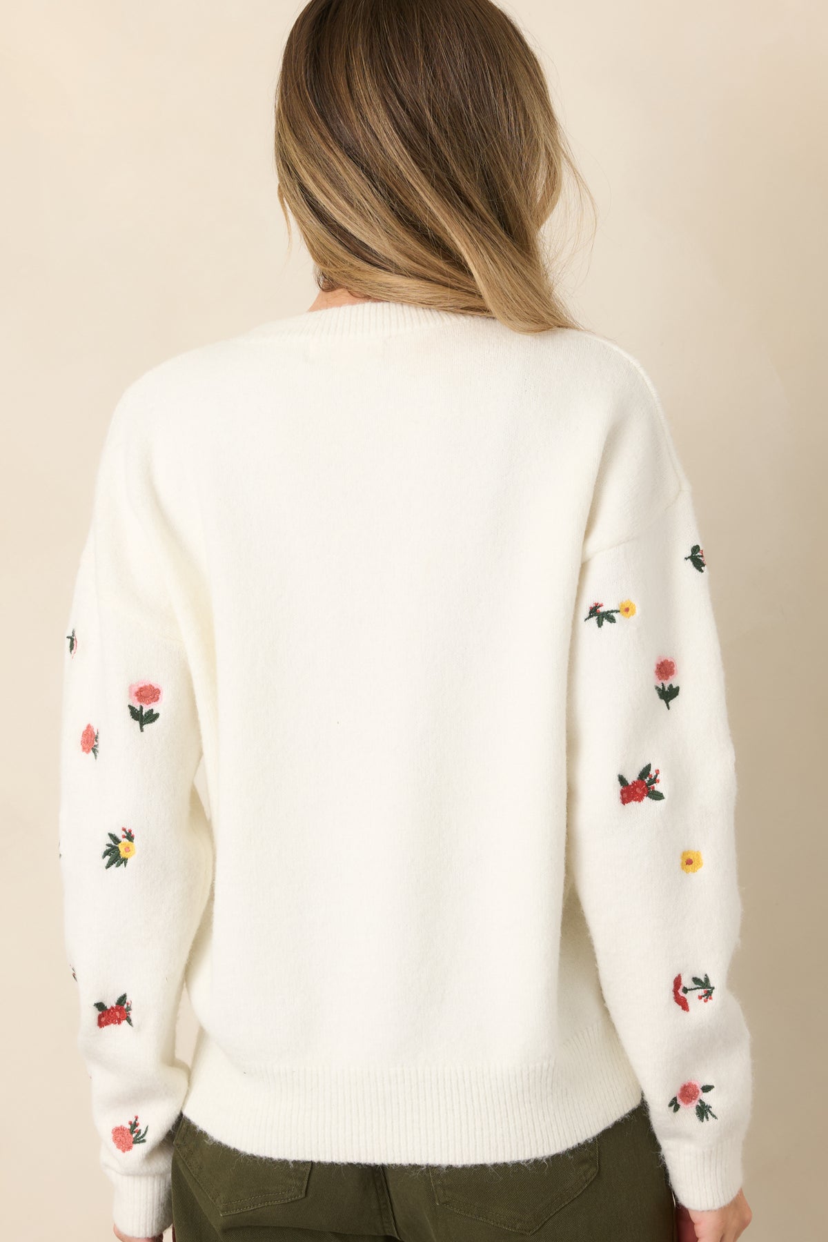 Rear view of the white knit sweater showcasing multicolor floral embroidery, long sleeves, and a ribbed hem.