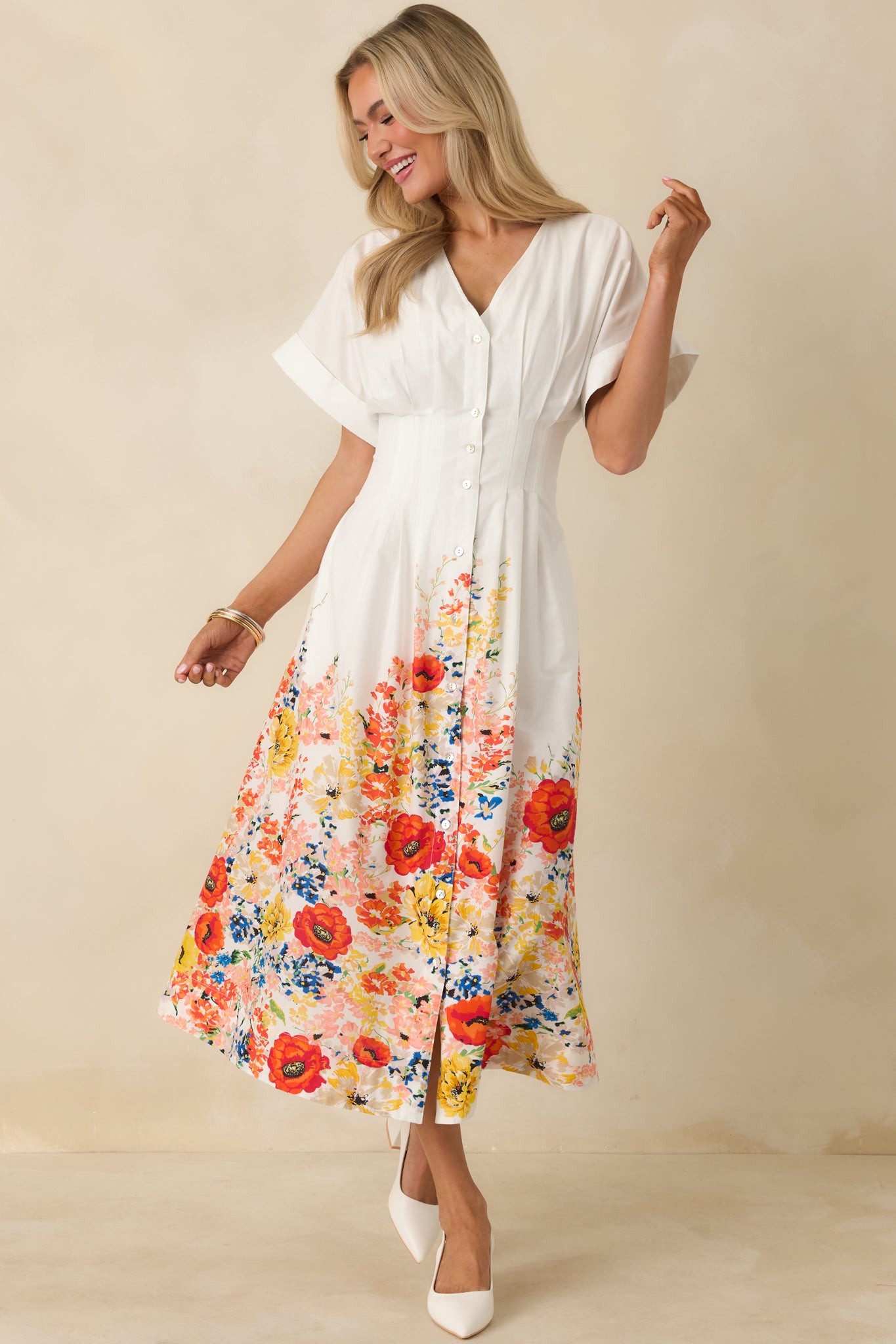 White cotton midi dress with a flowy skirt, V-neckline, short flutter sleeves, and a multicolor floral border print along the hem.