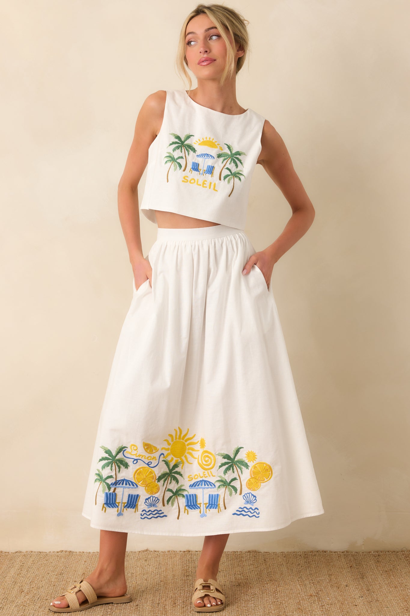 White midi skirt featuring vibrant embroidered sun, palm, and seaside motifs along the hem, designed with a full, flowy silhouette and soft structure.