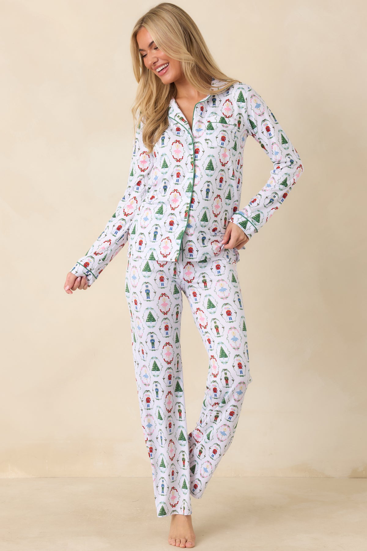 White pajama pants feature an allover nutcracker and holiday motif print with green piping and a relaxed wide-leg fit.