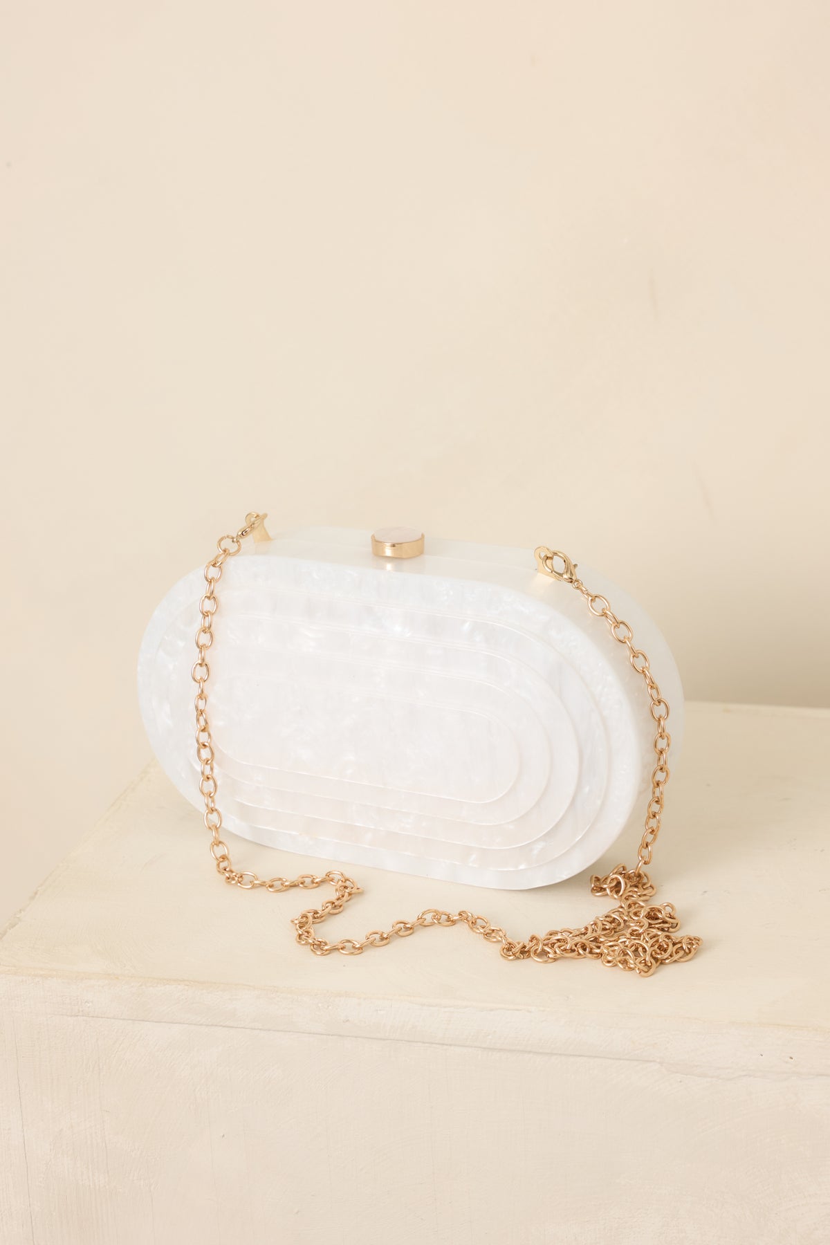 Elegant white pearlescent clutch showcasing its compact oval shape, sleek surface, top clasp closure, and detachable chain strap.