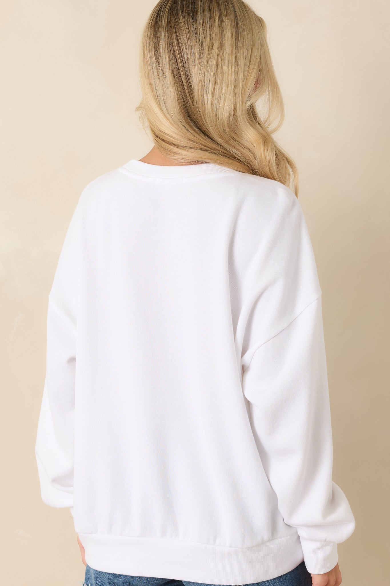 Back view of the white oversized sweatshirt featuring long sleeves, dropped shoulders, ribbed trim, and a relaxed fleece silhouette.