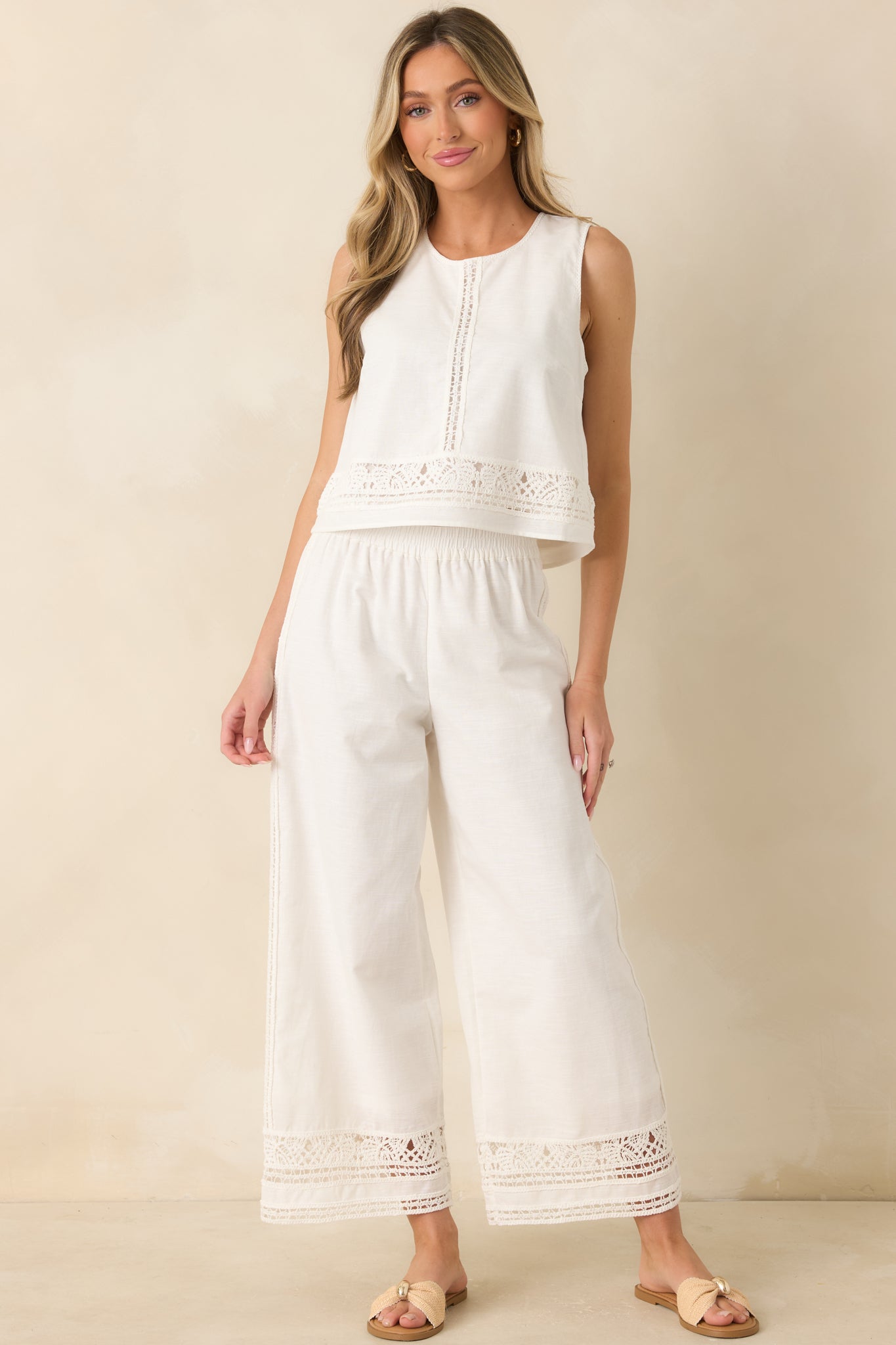 White sleeveless top crafted from a breathable cotton-linen blend, featuring a round neckline, crochet-inspired embroidered trim, and a relaxed silhouette.