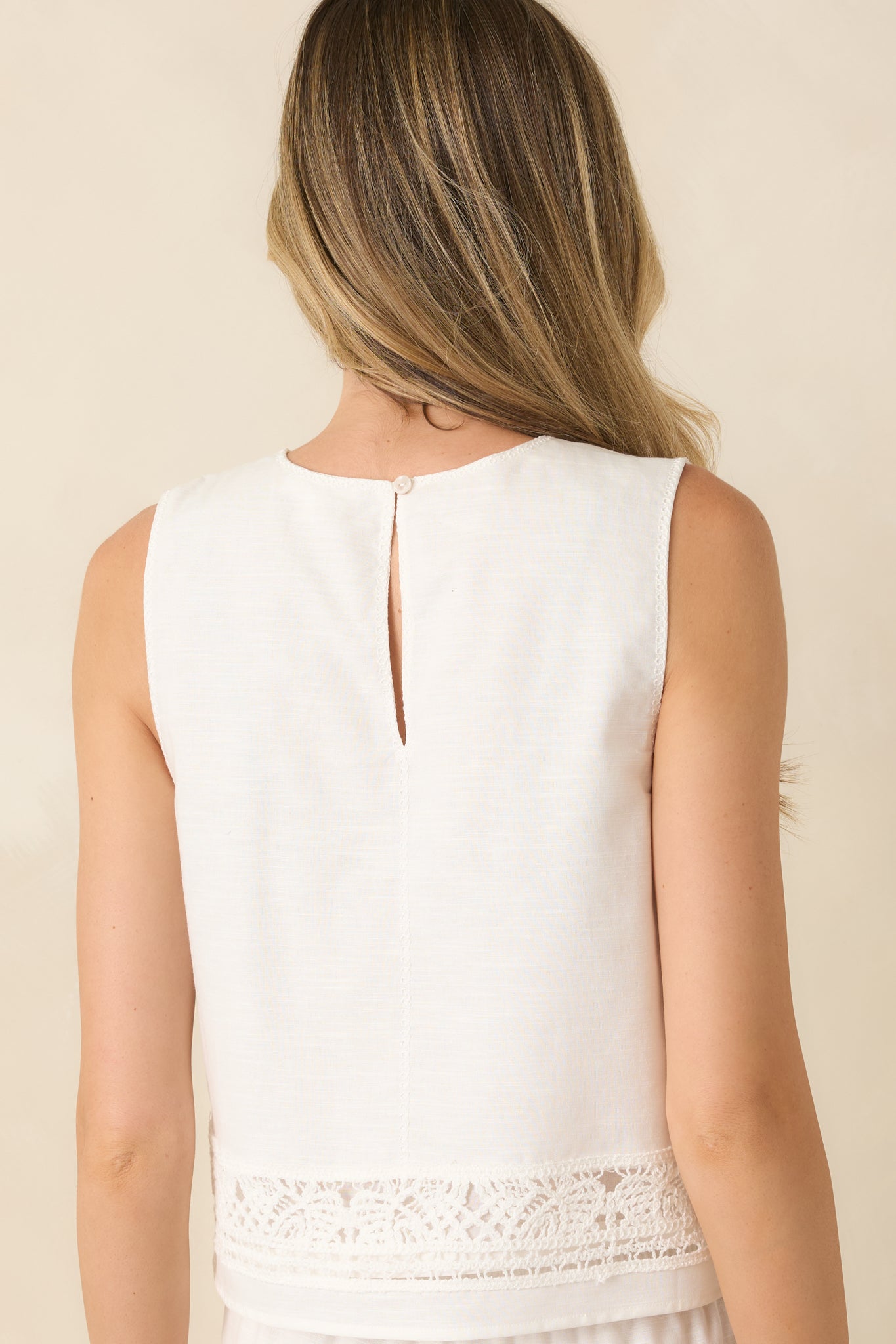 Back view of the white sleeveless top featuring a relaxed fit and a keyhole button closure at the neckline.