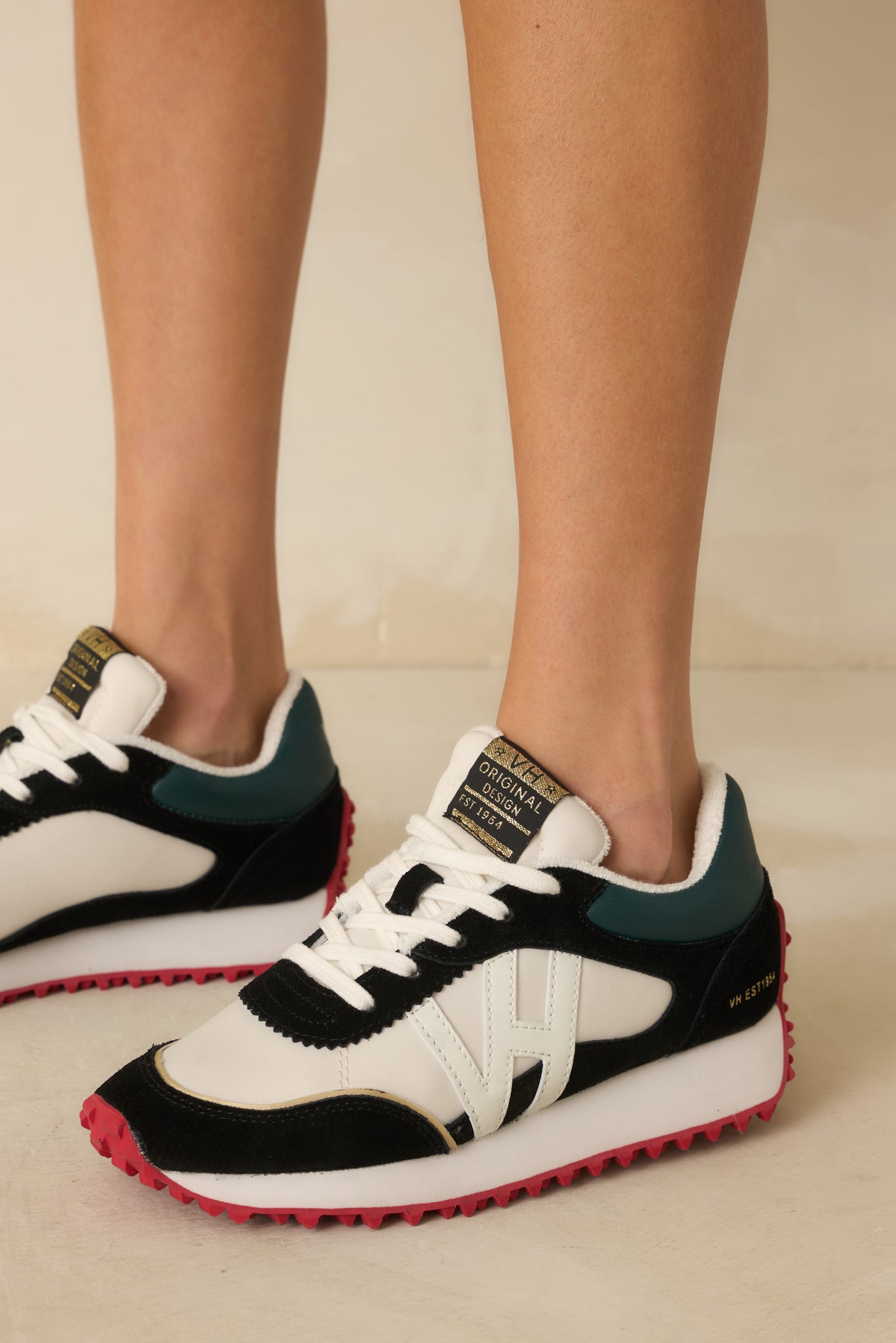 White sneakers with black faux suede panels and a bold red spiked sole for a standout look.