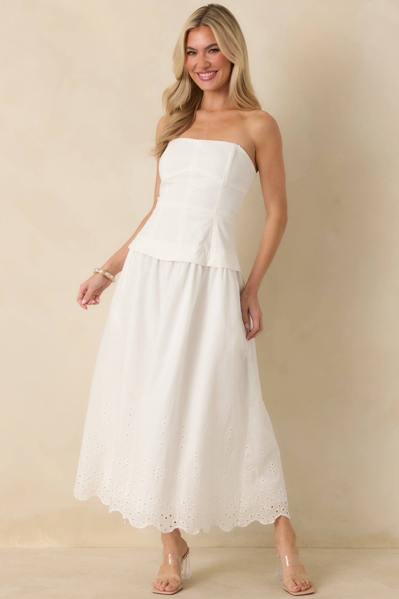 Full-length front view of a white strapless midi dress showcasing the structured seamed bodice, defined waist seam, and softly flared cotton skirt with eyelet lace hem.