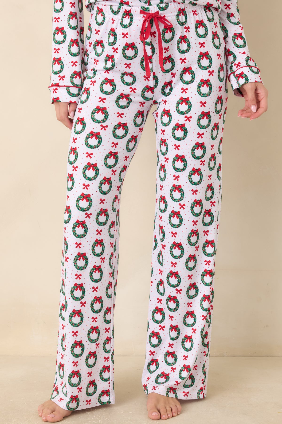 White pajama pants feature an allover wreath and bow print with a relaxed fit and contrasting black piping along the edges.